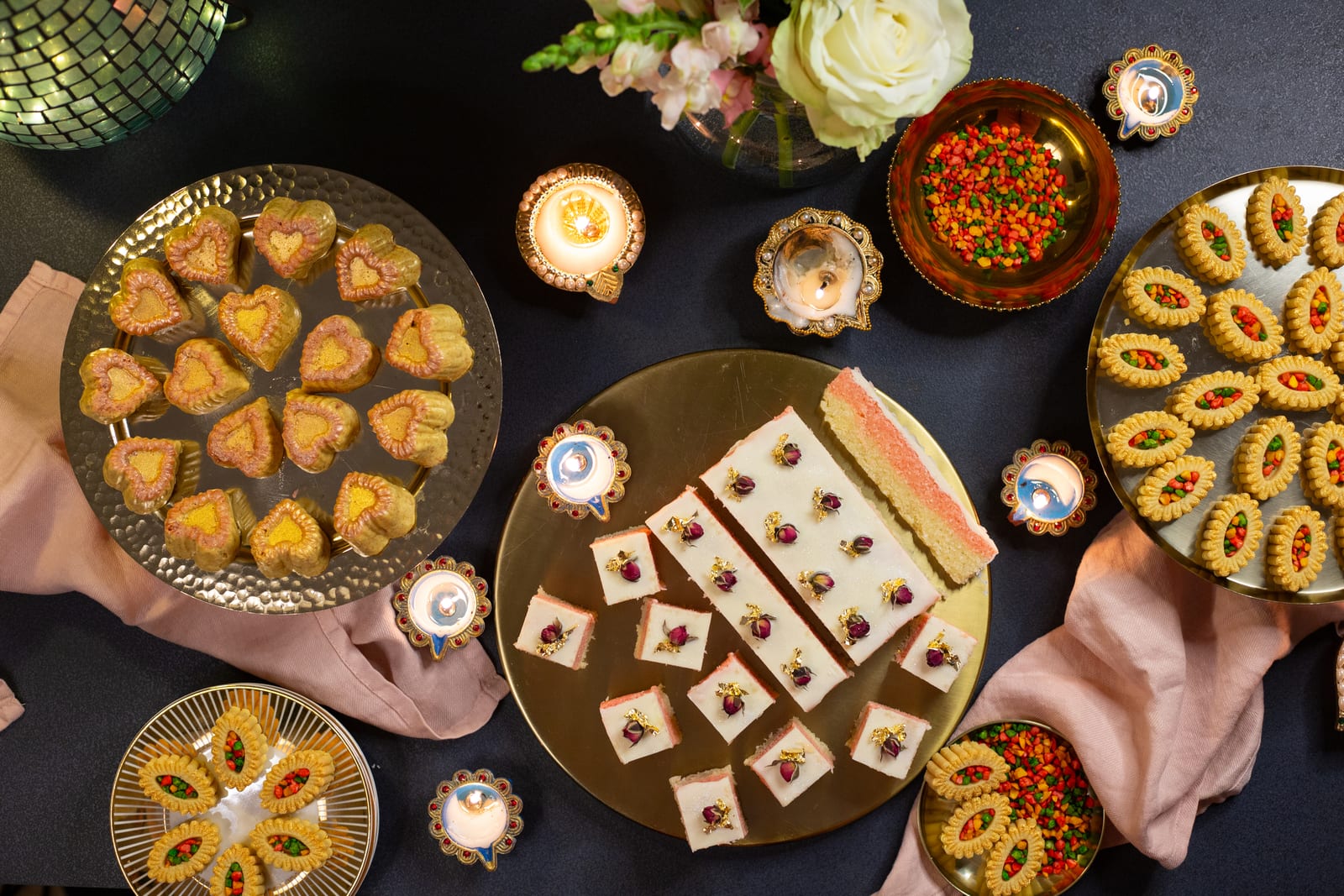 Diwali sweetmeats on gold platters with diyas, from above