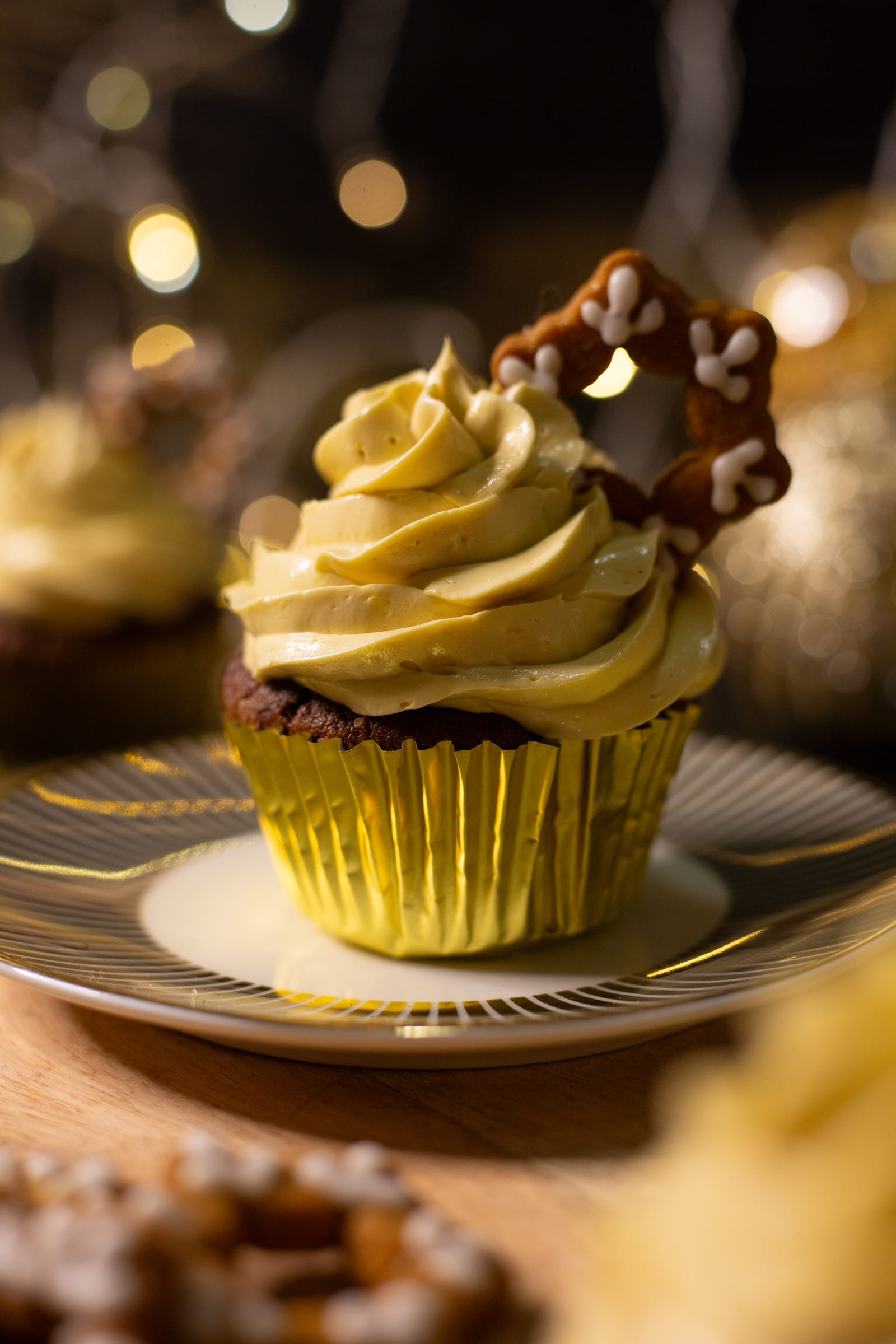 A gingerbread cupcake with a swirl of eggnog buttercream and an iced pretzel star on a gold plate