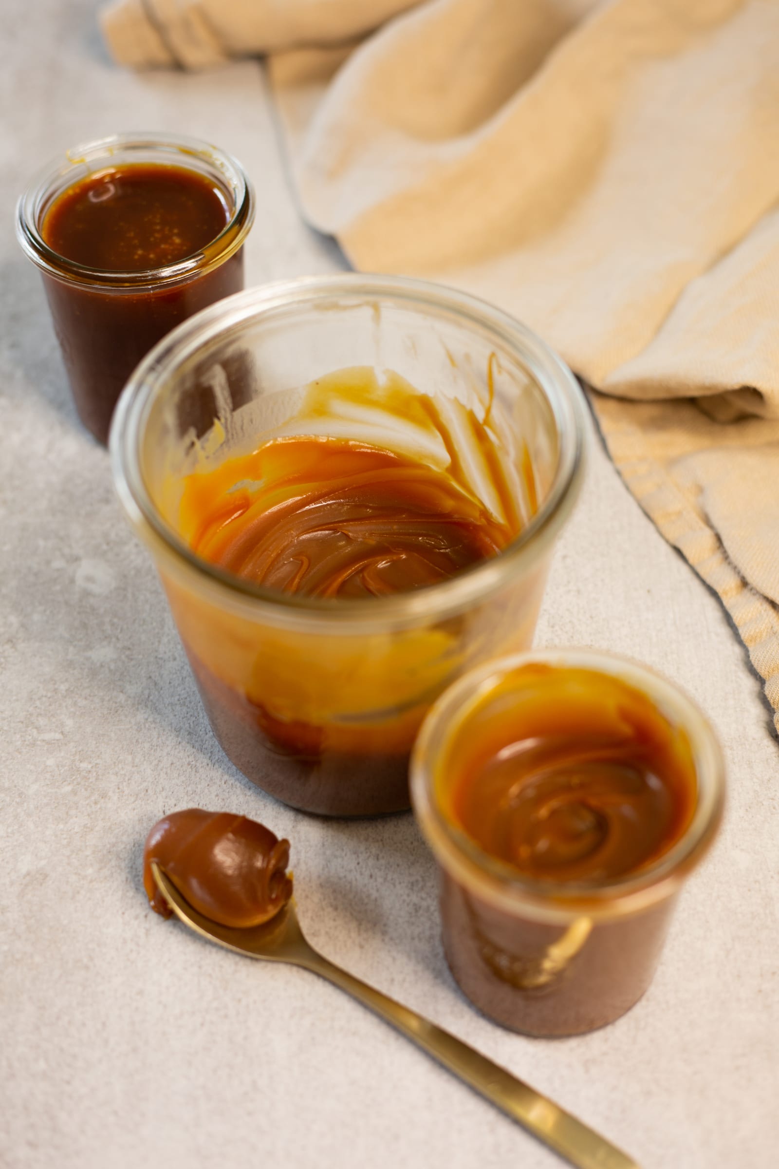 Jars of salted caramel sauce with caramel dripping down the glass and a gold spoon