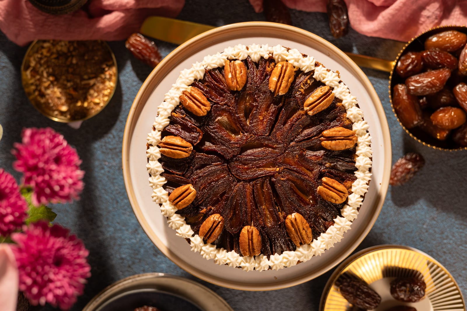 A sticky date and pecan cake from above, with pink flowers and dates