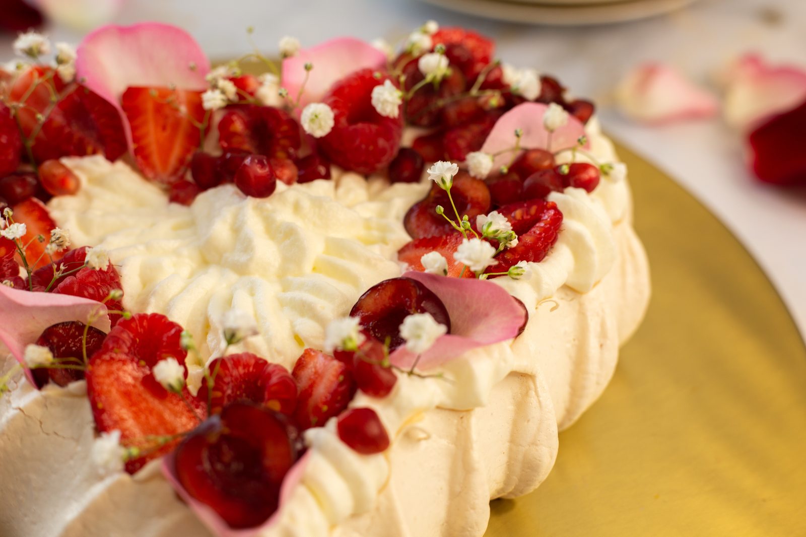 Whipped cream, berries, rose petals and baby's breath on a berry pavlova, close up from a low angle