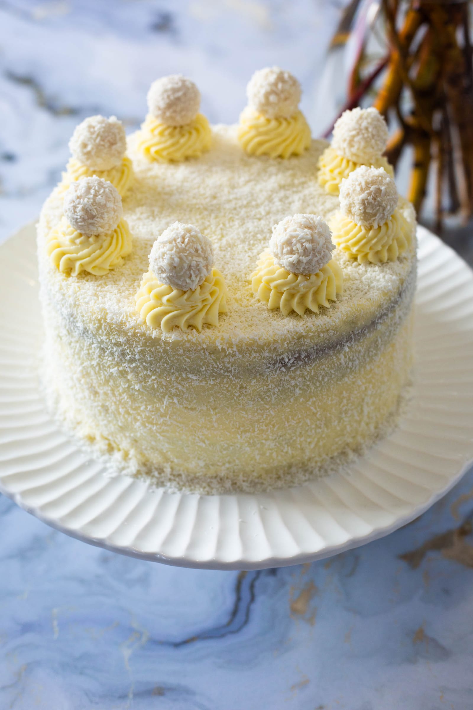 A whole Raffaello cake on a white fluted plate on blue marble, from slightly above