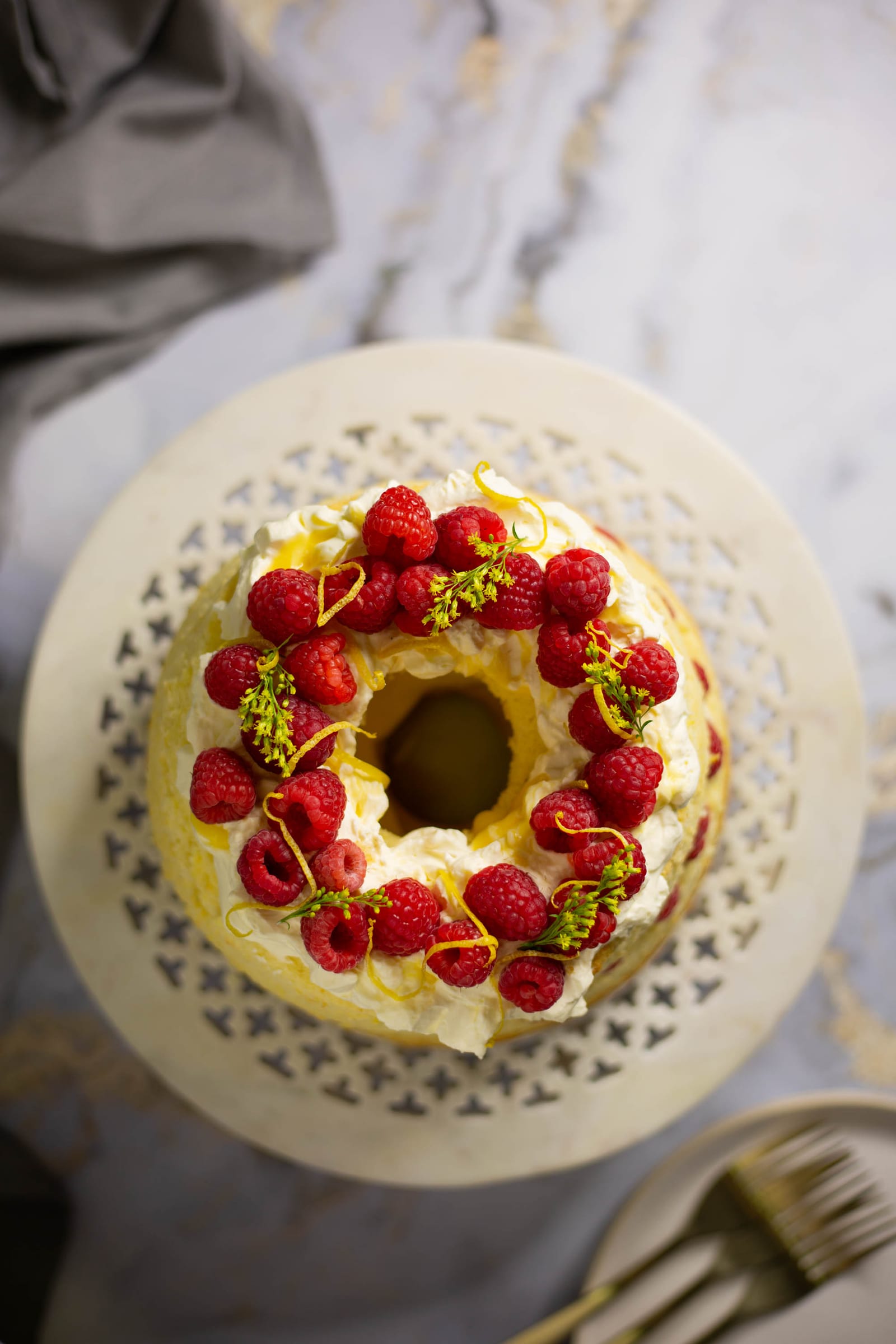 A whole lemon curd and raspberry chiffon cake on a white pierced cake stand, from above