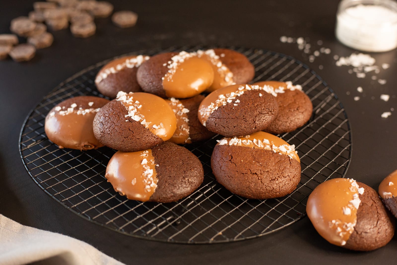 Rye brownie cookies dipped in milk chocolate and flaky salt, cooling on a wire rack