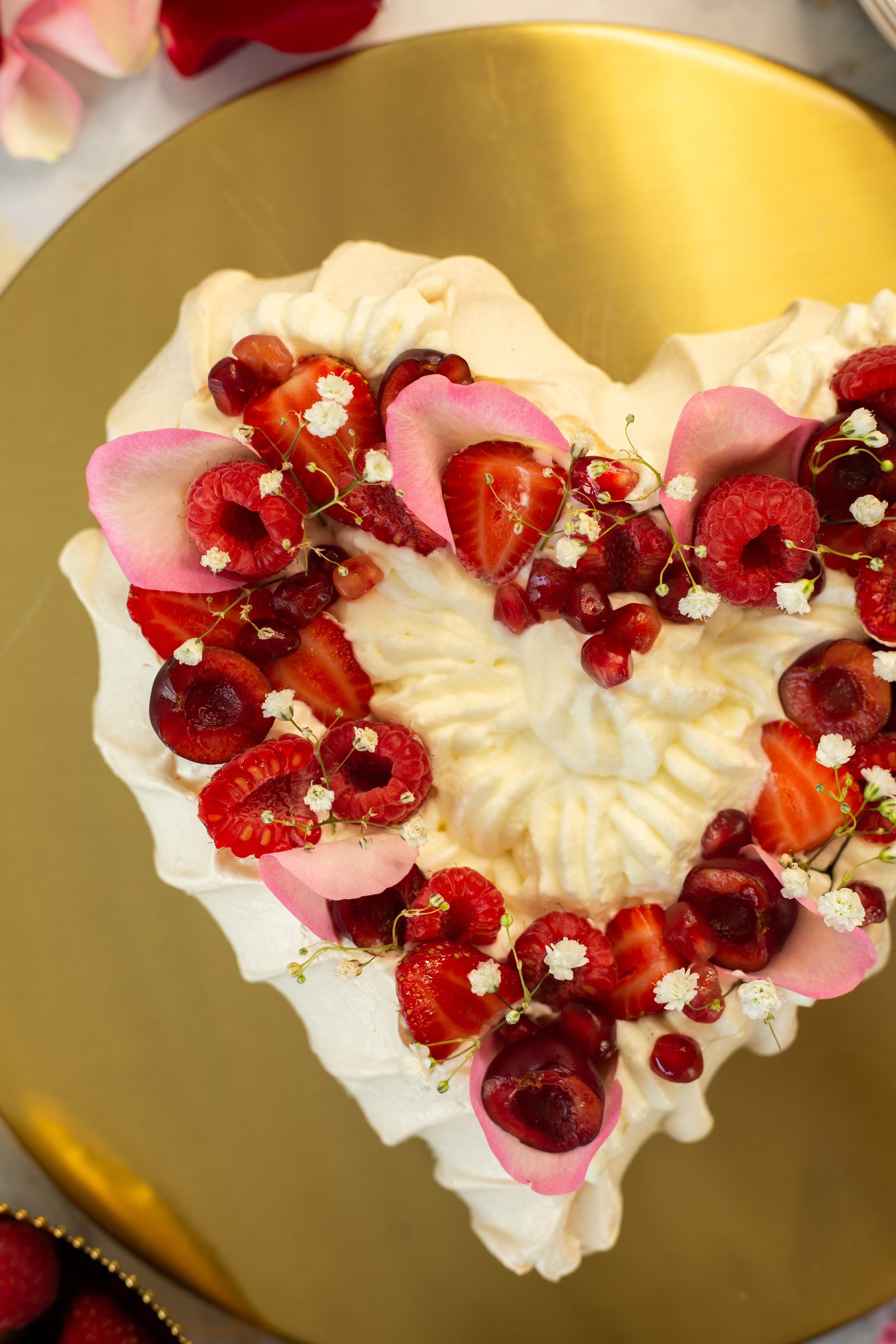 Strawberries, cherries, pomegranate and rose petals on the whipped cream of a berry pavlova, close up from above