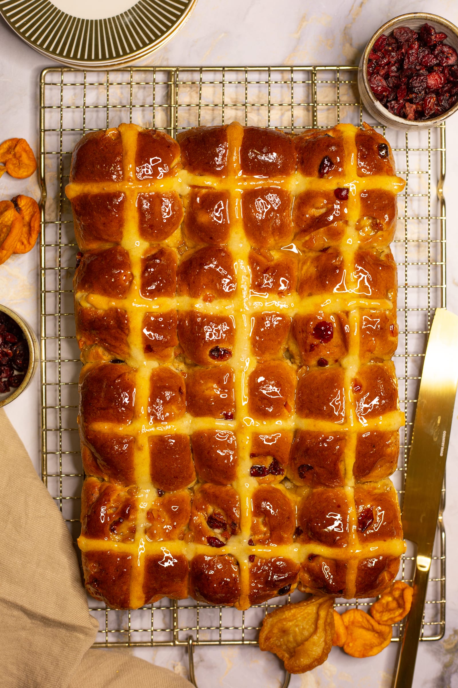 A whole tray of glazed Turkish apricot and cranberry hot cross buns on a wire rack