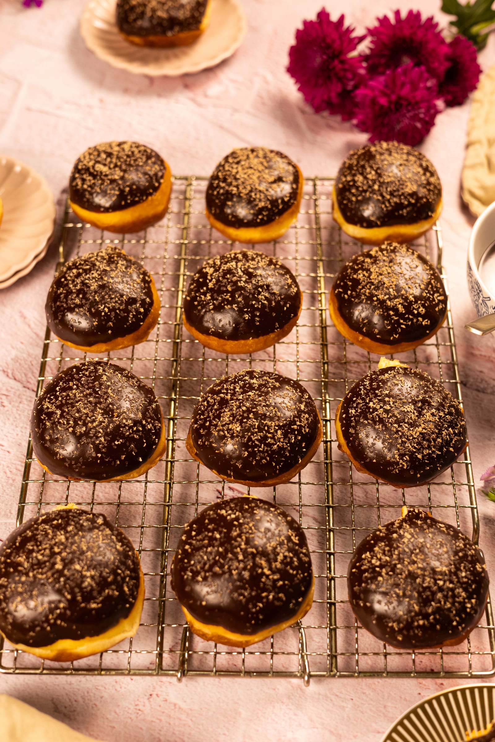 A rack of chocolate-glazed brioche donuts with magenta flowers