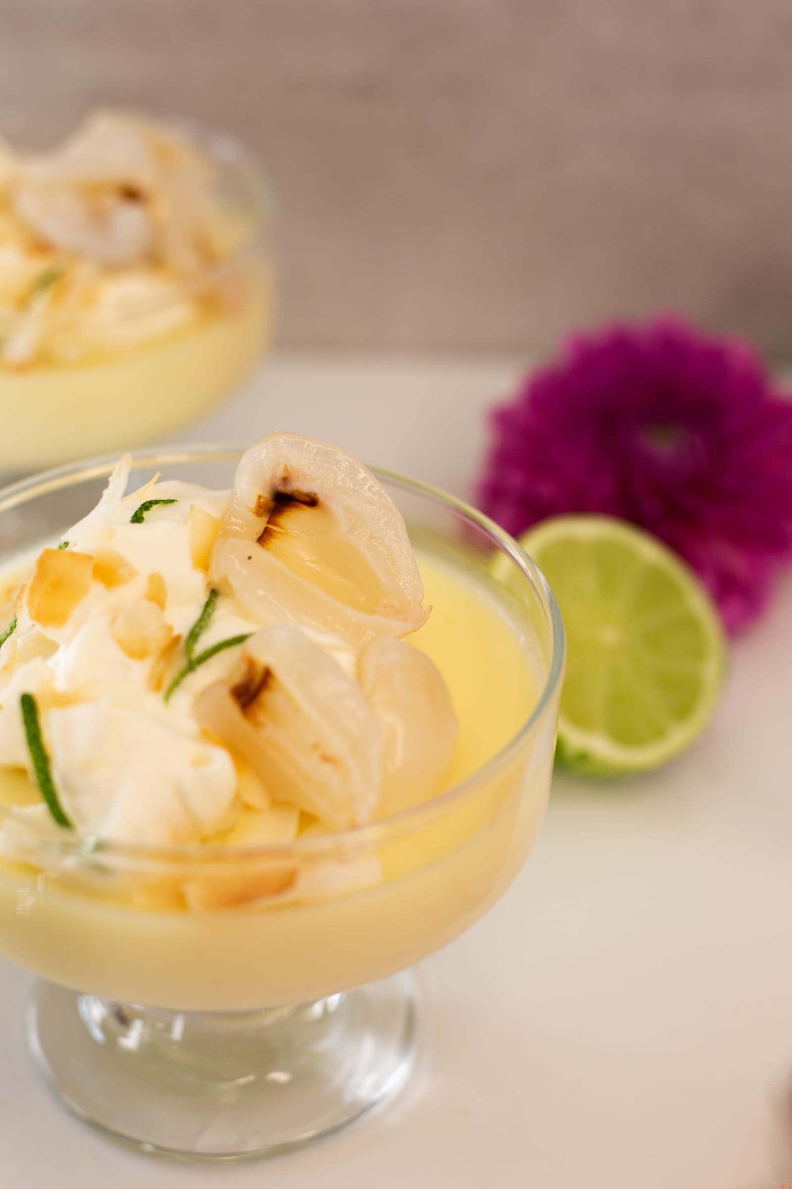 Close-up of whipped cream, a litchi and toasted coconut flakes on a lime and coconut posset