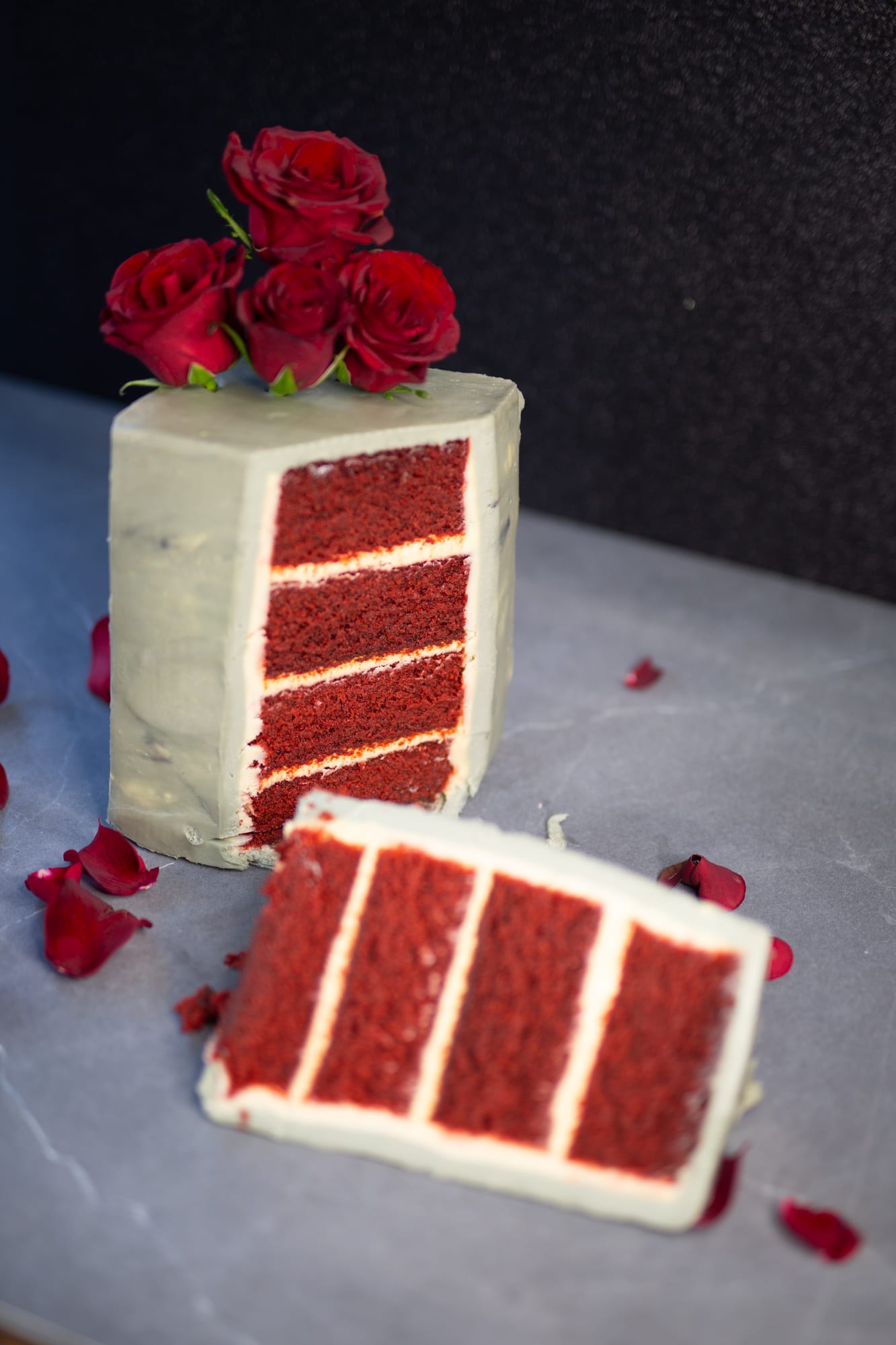 The four red layers of a cut decadent red velvet cake with a slice lying in front