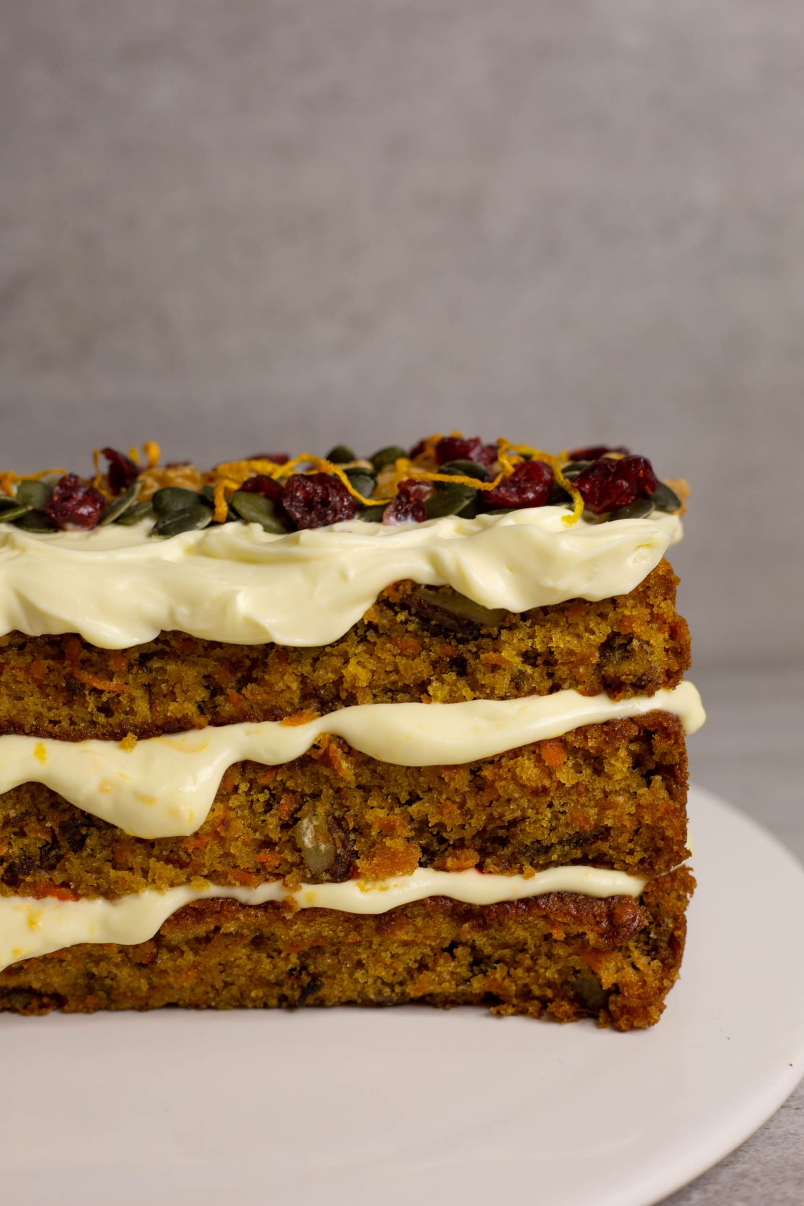 The three layers of carrot cake with orange cream cheese icing, topped with walnuts, cranberries and seeds