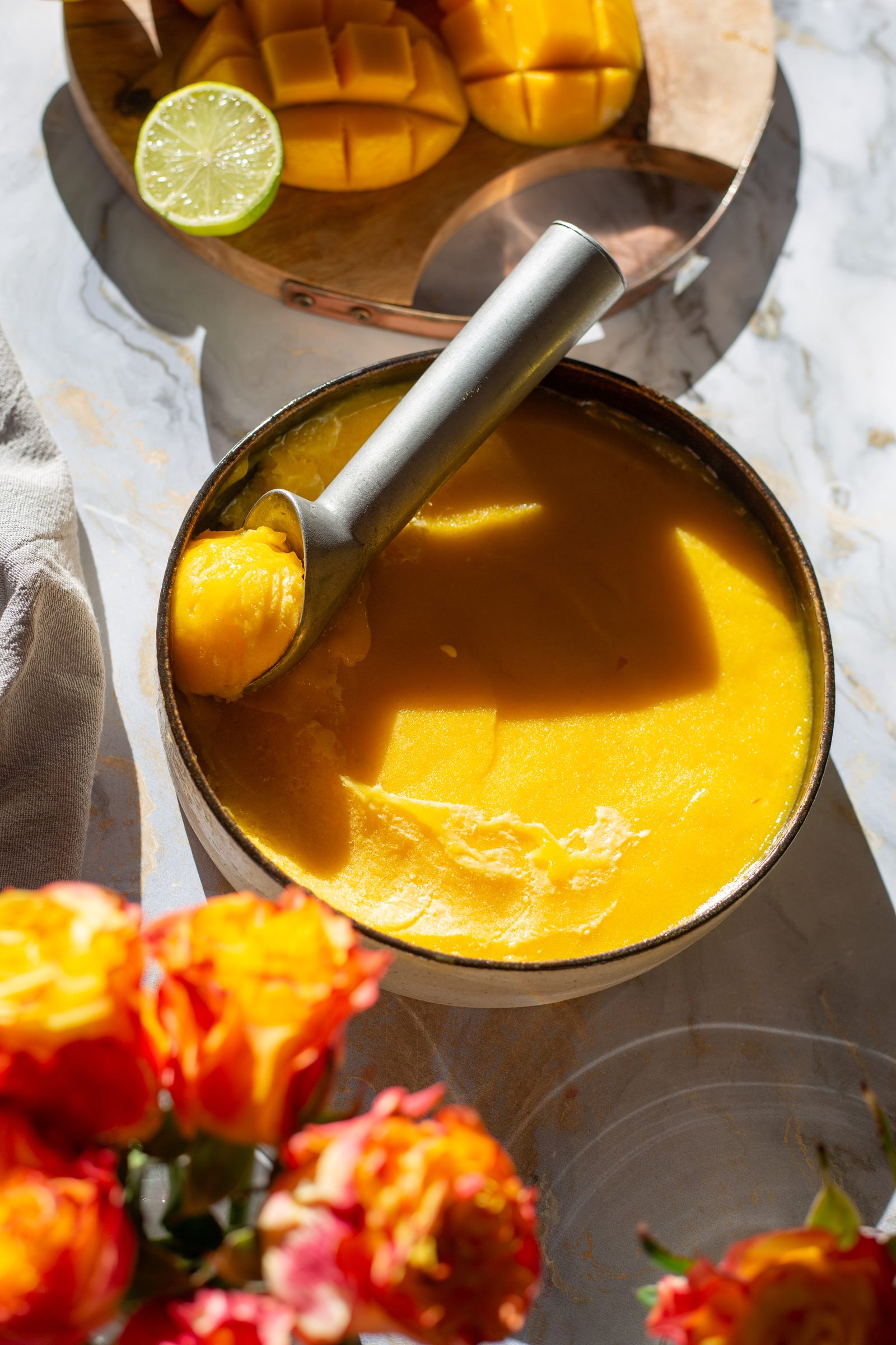 A dish of mango and chilli sorbet from above, with a cut mango and a lime behind