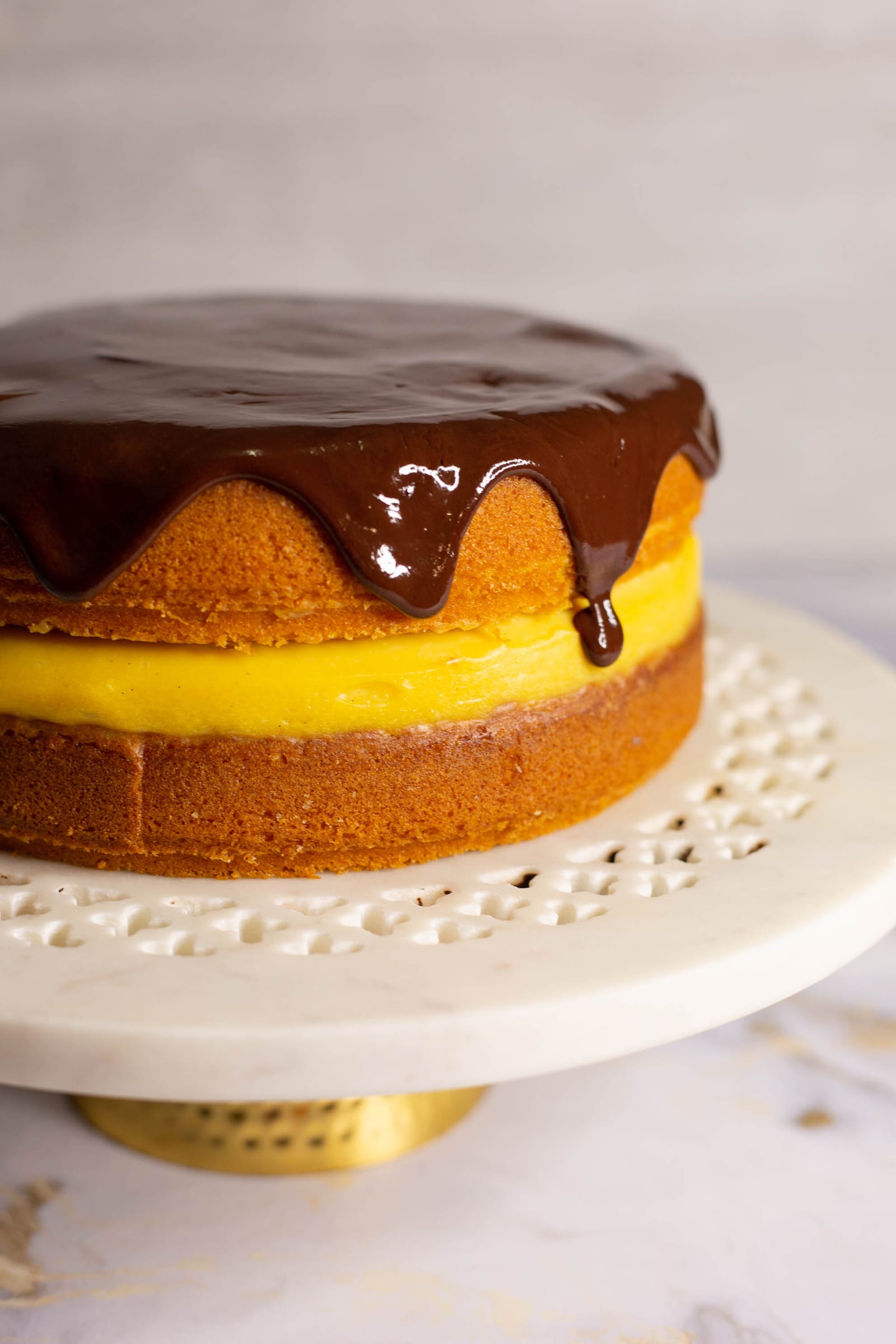 A whole Boston cream pie with dark chocolate ganache dripping over the vanilla sponge and custard