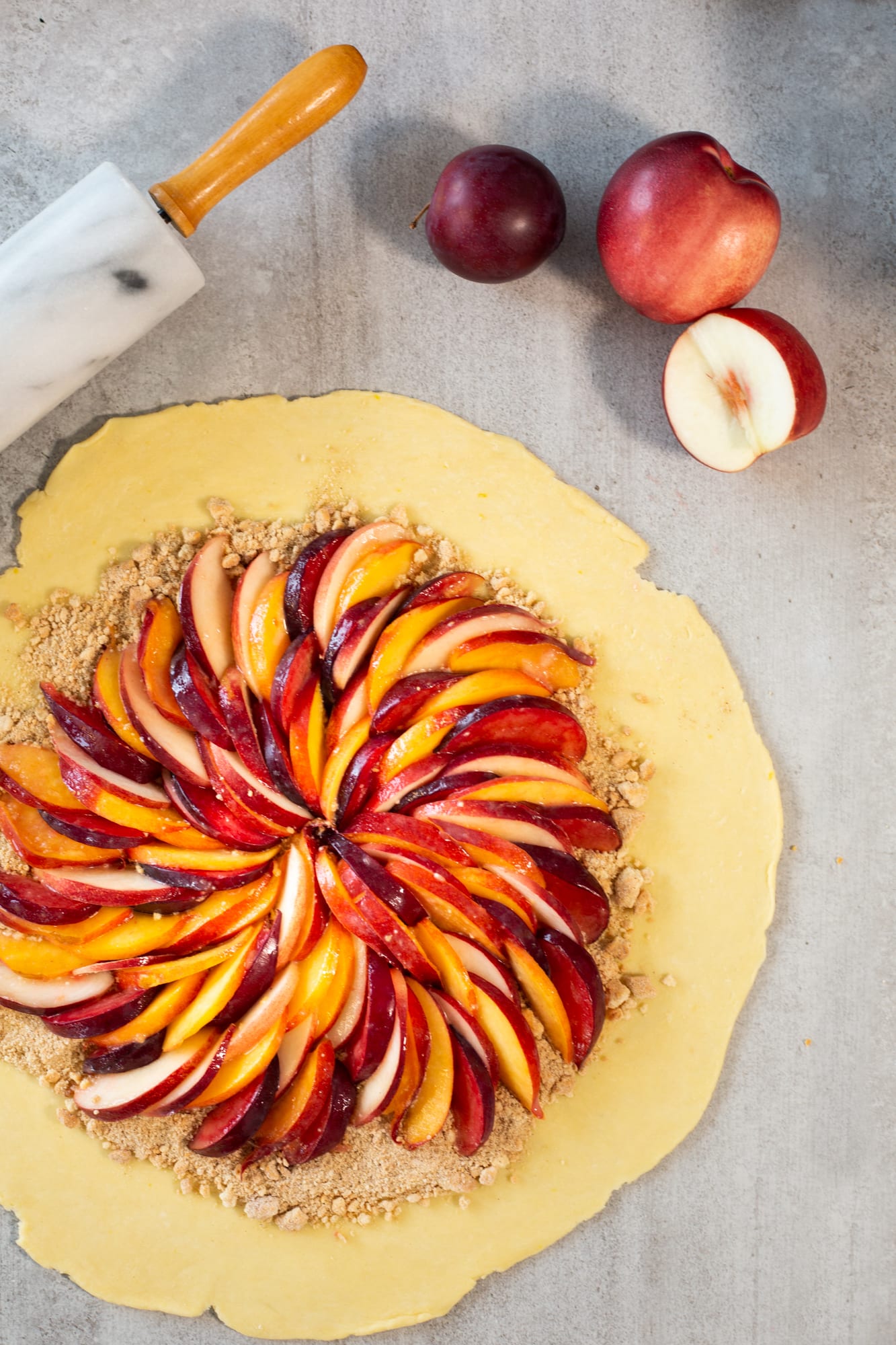 Slices of stone fruit arranged in a spiral on the rolled-out pastry, from above