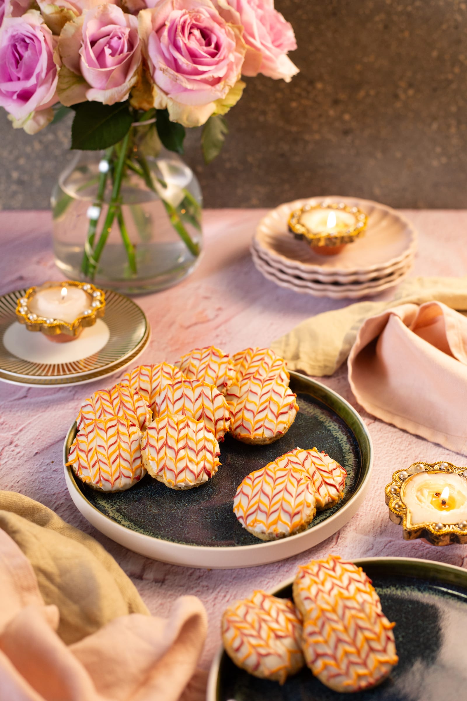 Coconut and almond biscuits on a plate, with pink roses and a lit diya
