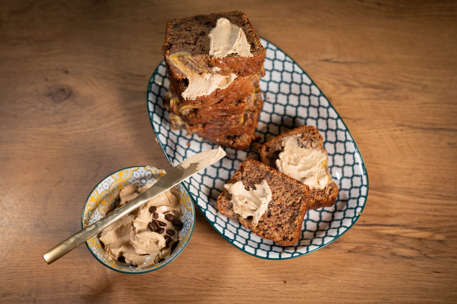 Buttered slices of banana and pecan nut bread on a patterned dish beside the butter bowl, from above