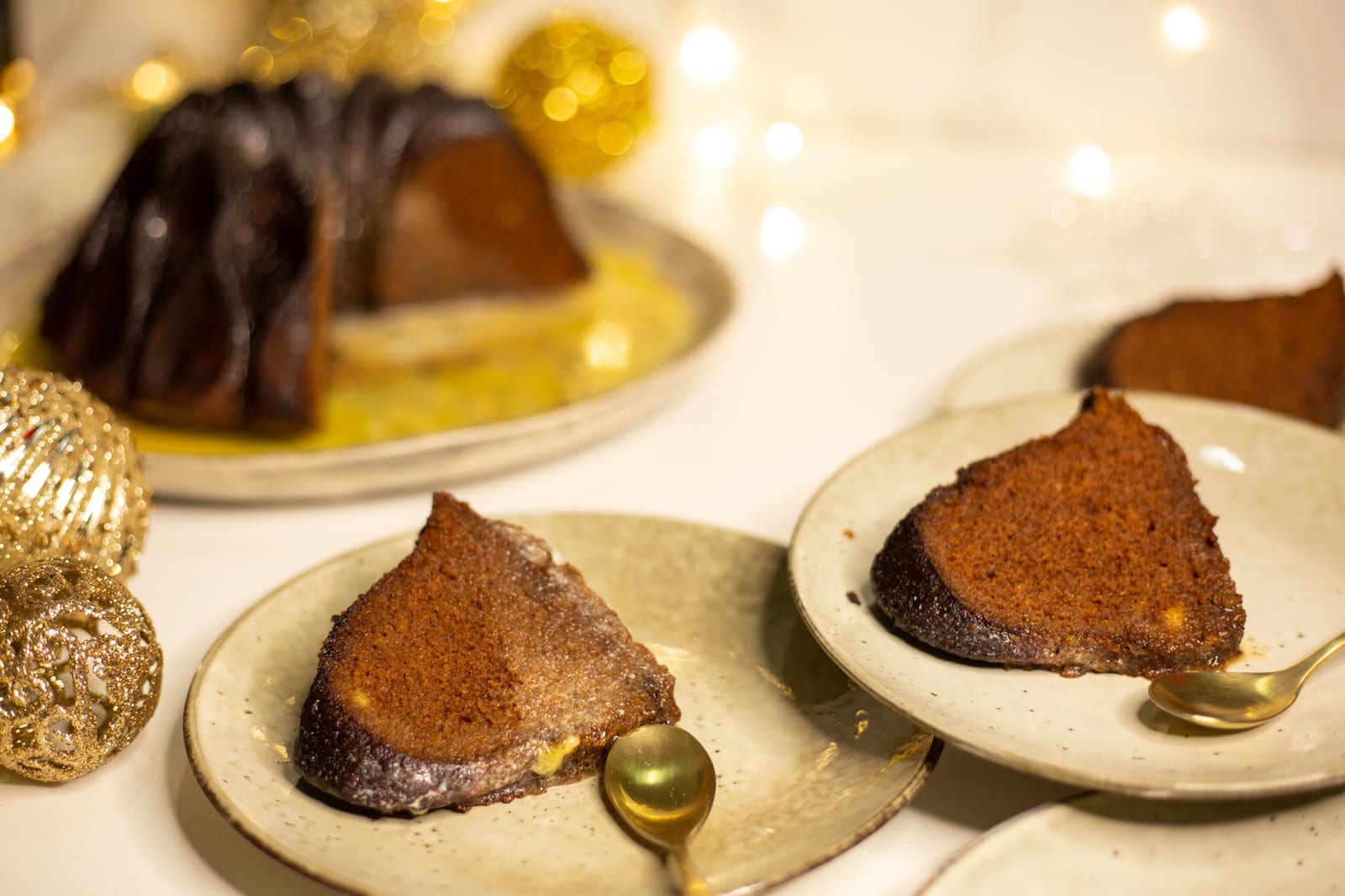 Slices of gingerbread pudding with custard, beside the bundt pudding and gold baubles