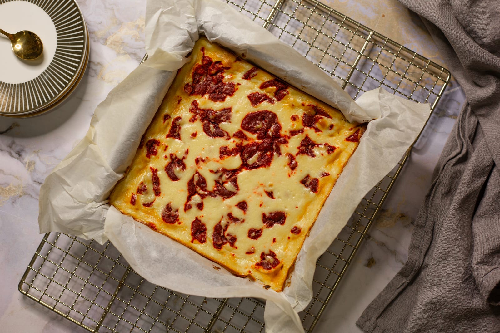 The whole slab of red velvet cheesecake blondies in its baking paper on a cooling rack, from above