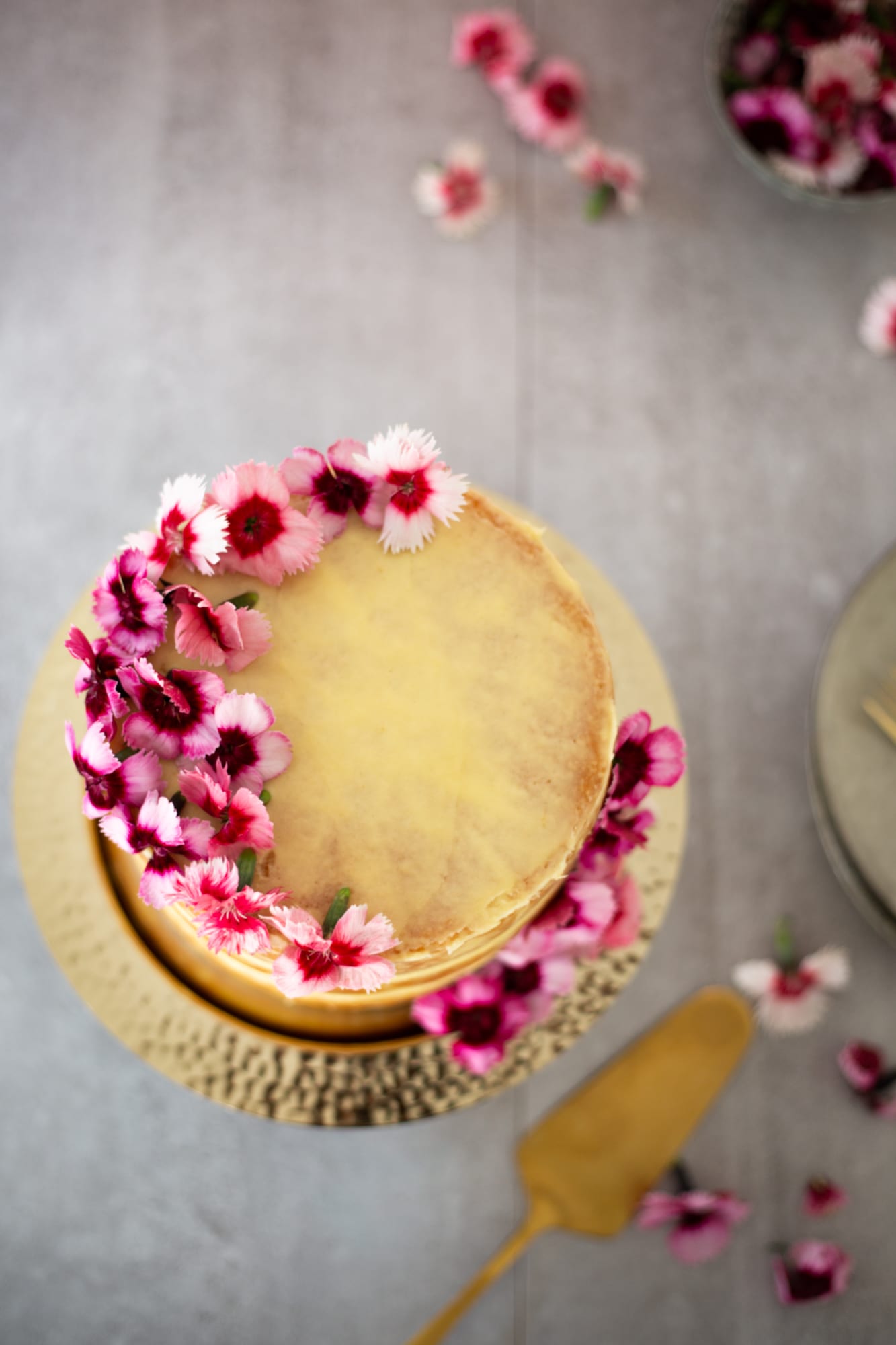 A lemon curd cake on a gold stand with flowers around it, from above