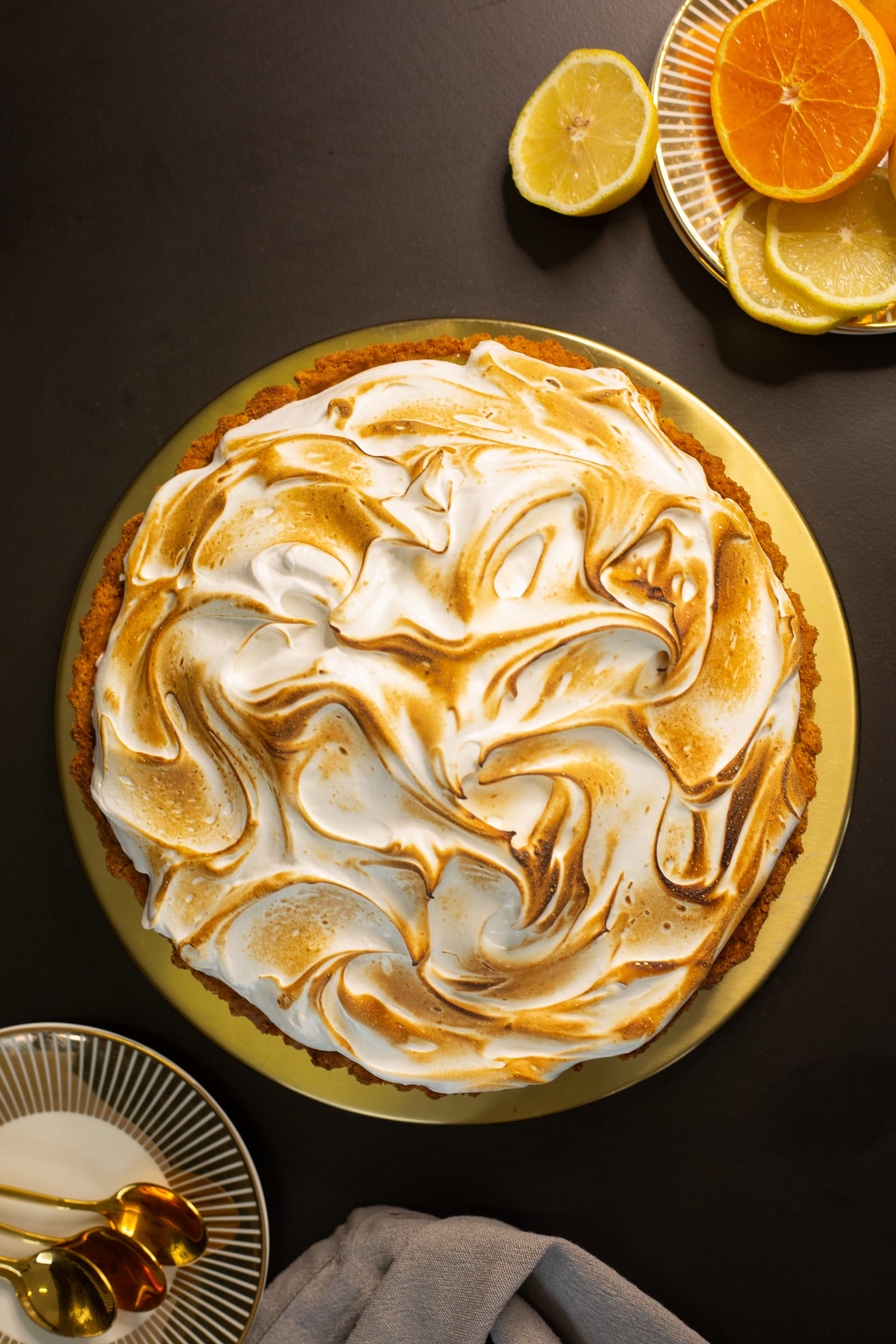 The whole lemon meringue pie from above, with lemons and oranges alongside