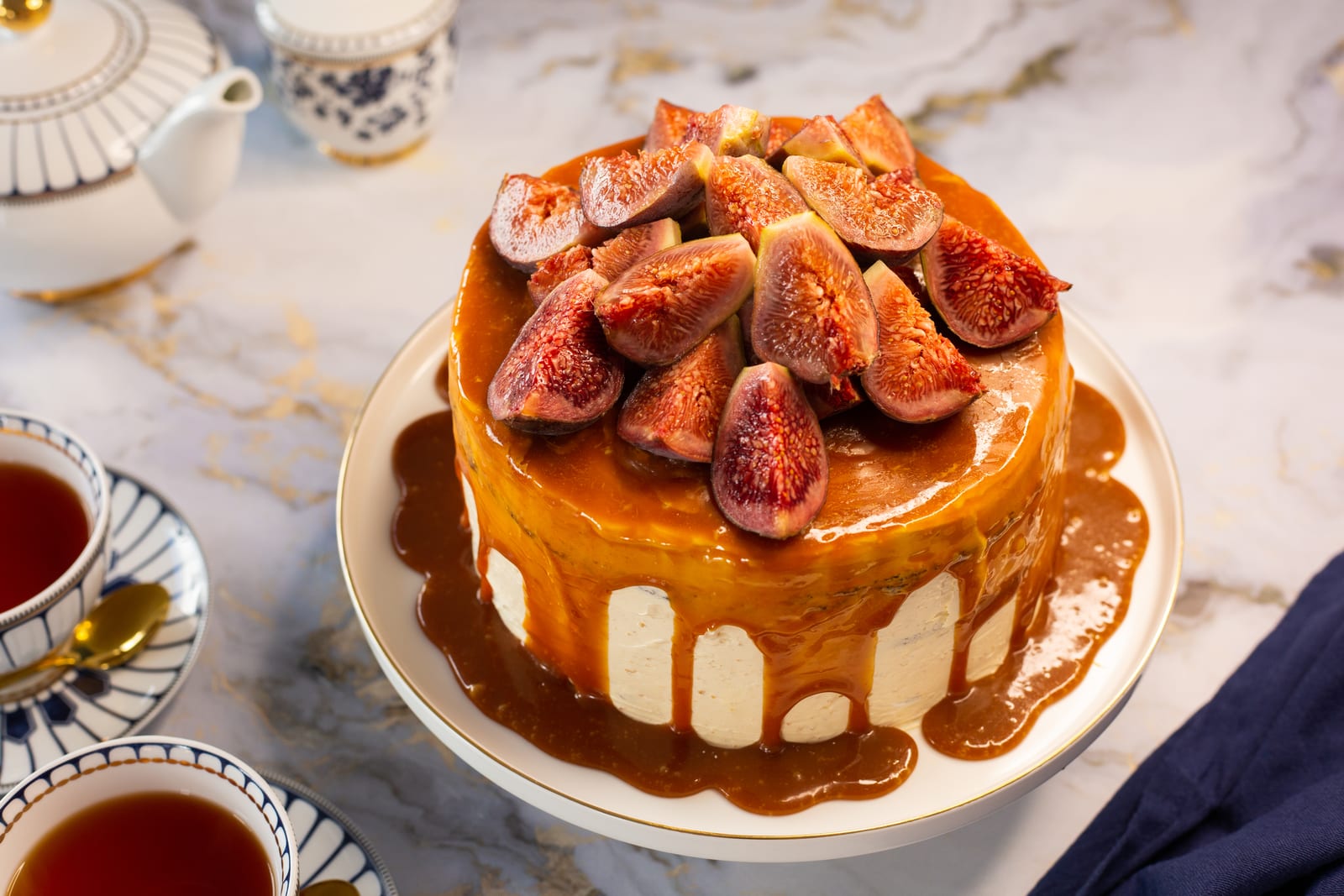 Devil's food cake with hazelnut buttercream, caramel and figs on a cake stand, surrounded by teacups