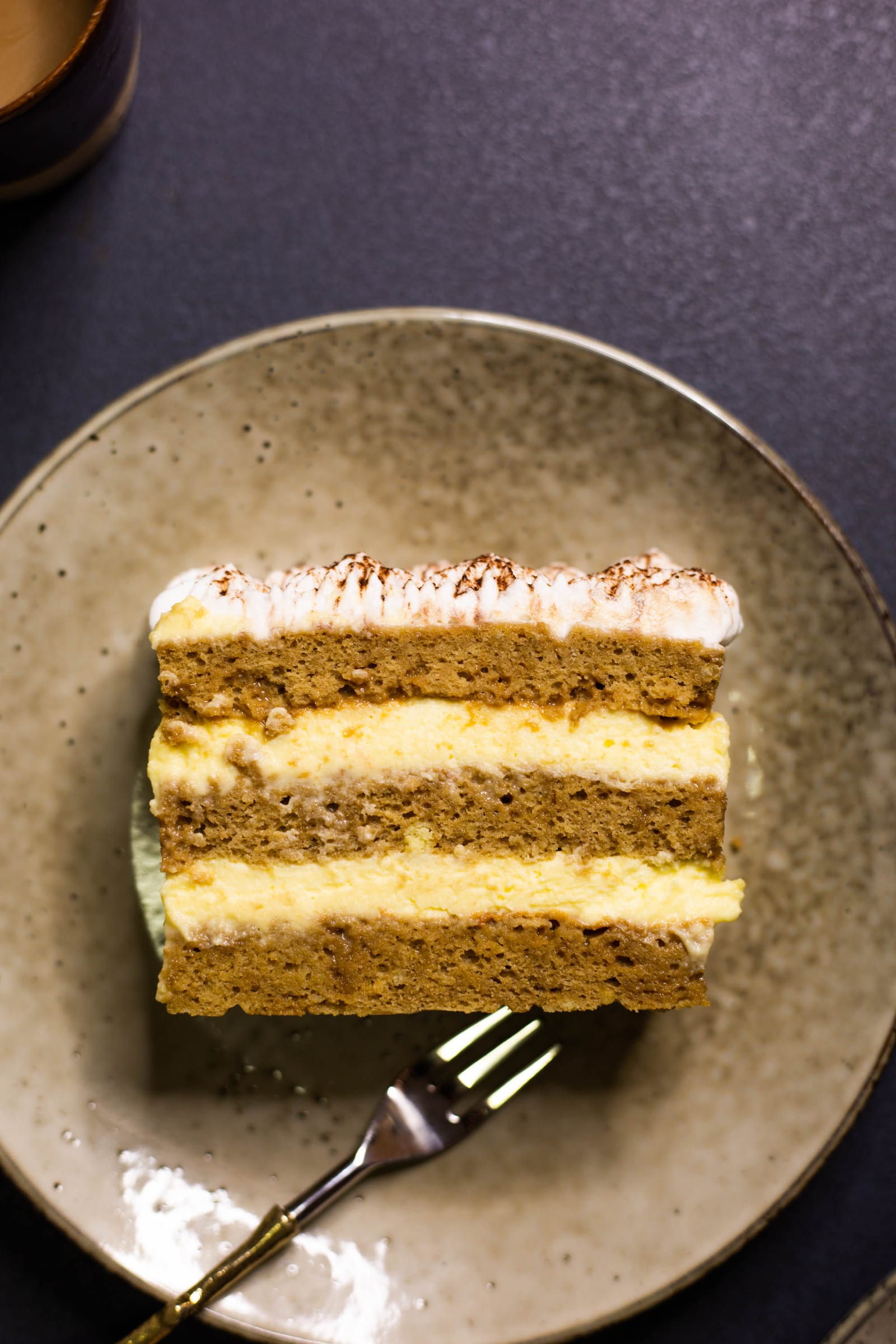 A slice of tiramisu tres leches cake with a gold fork, from above