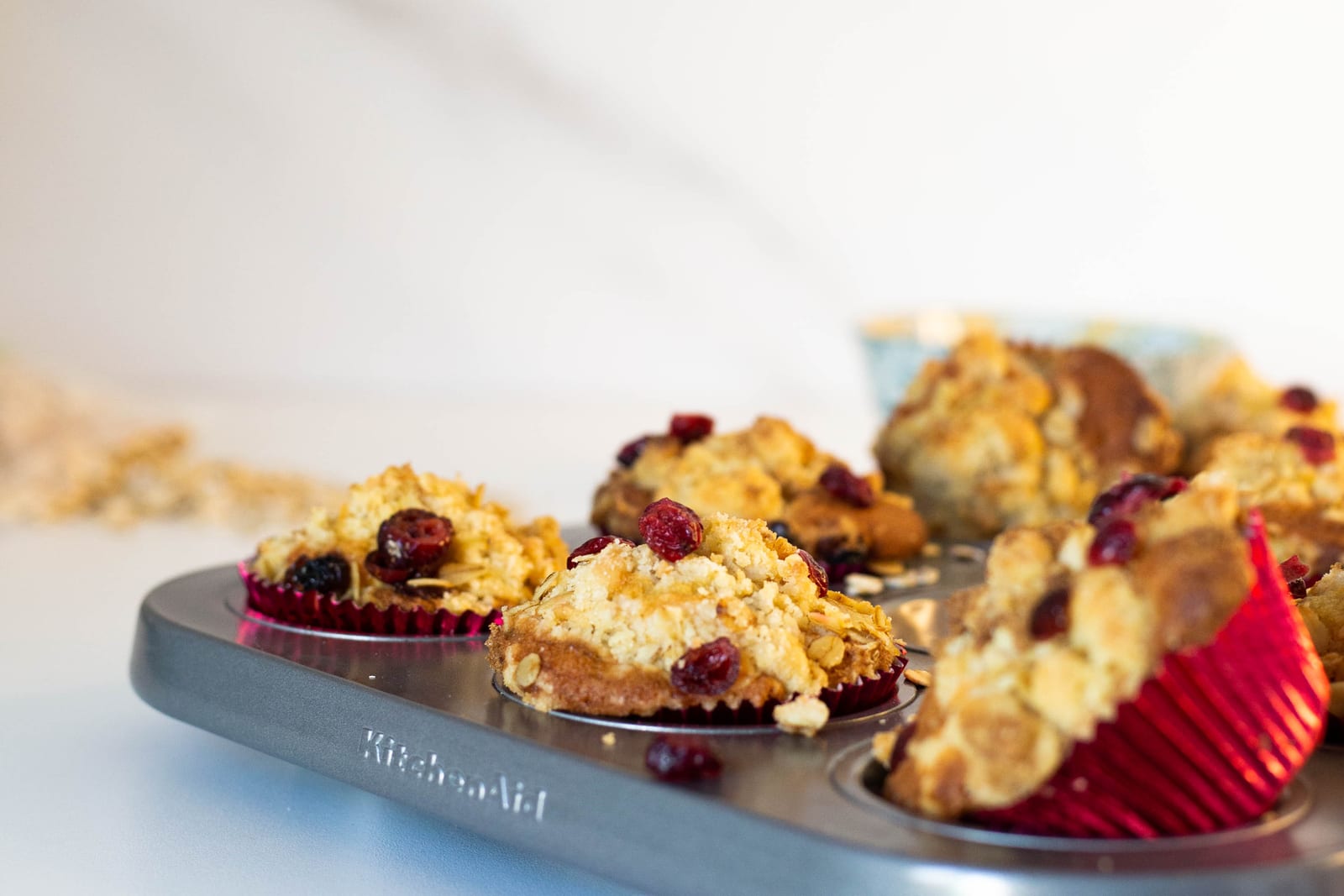 Cranberry crumble muffins in their tin, one tipped over in its red case