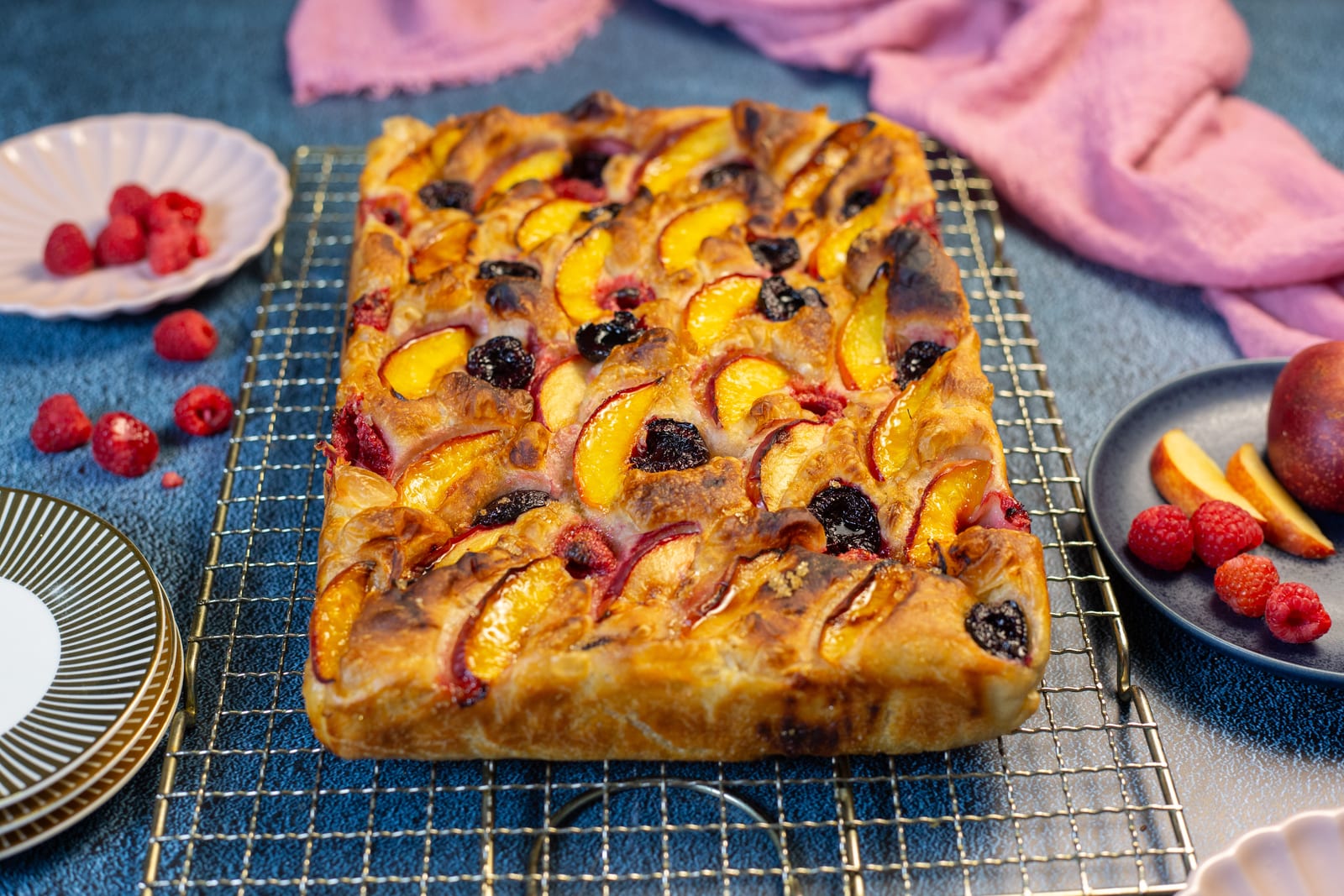 A nectarine and cherry focaccia on a wire rack, with pink linen and fruit