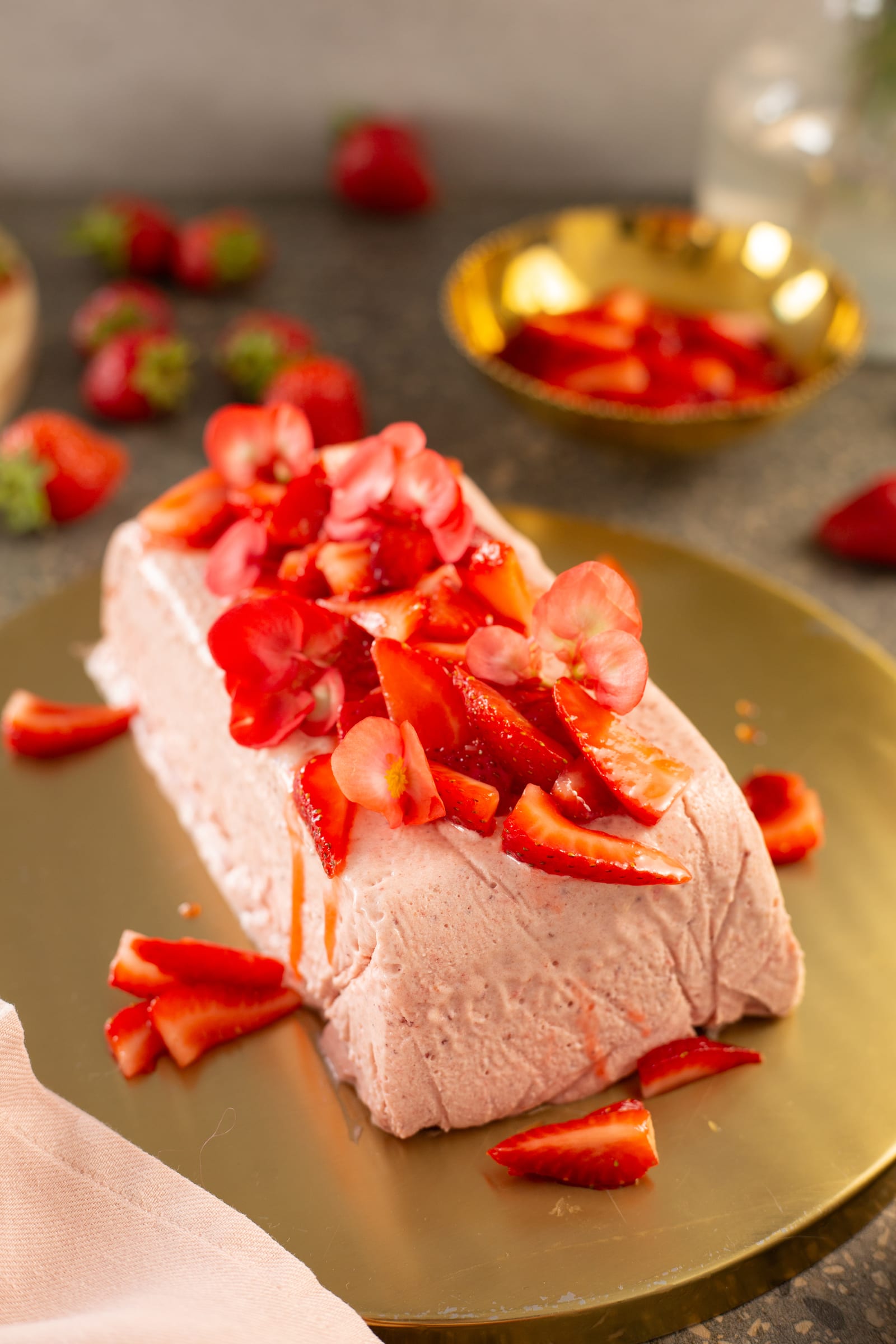 A whole roasted strawberry and rosemary semifreddo at an angle beside a gold bowl of strawberries