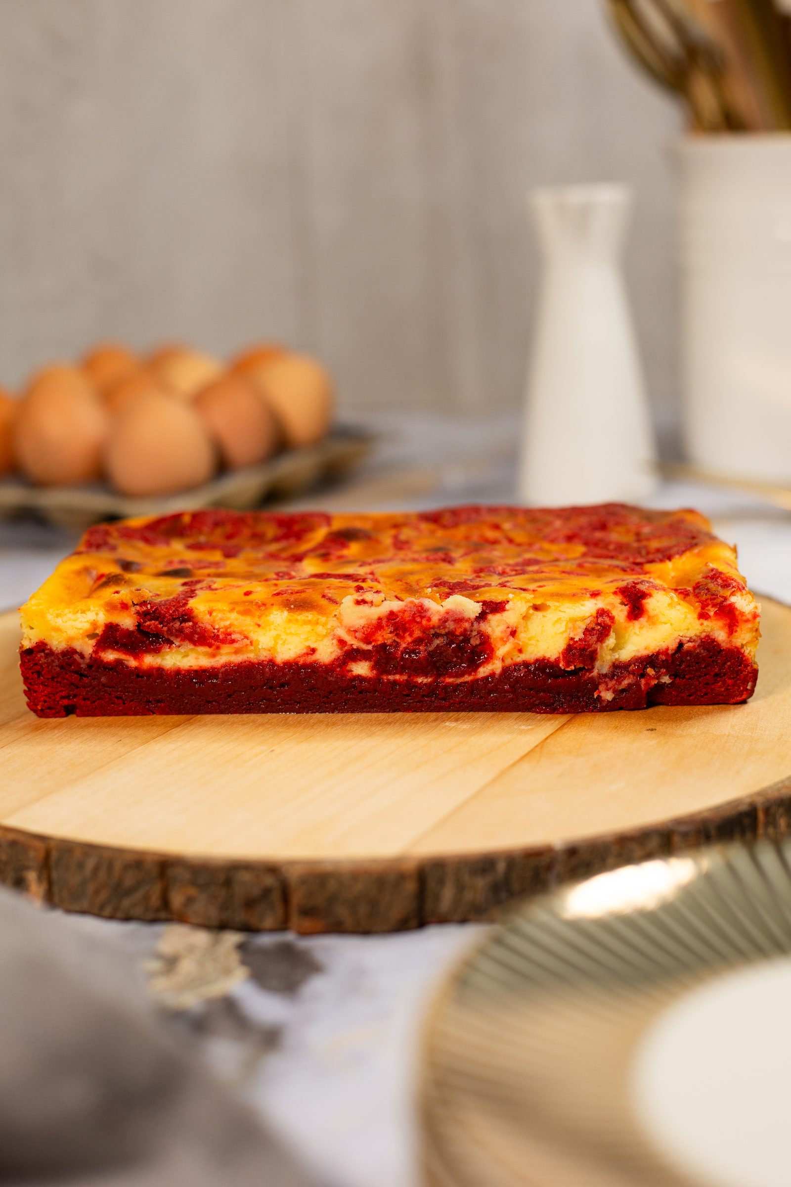 The uncut slab of red velvet cheesecake blondies on a wooden board, from the side