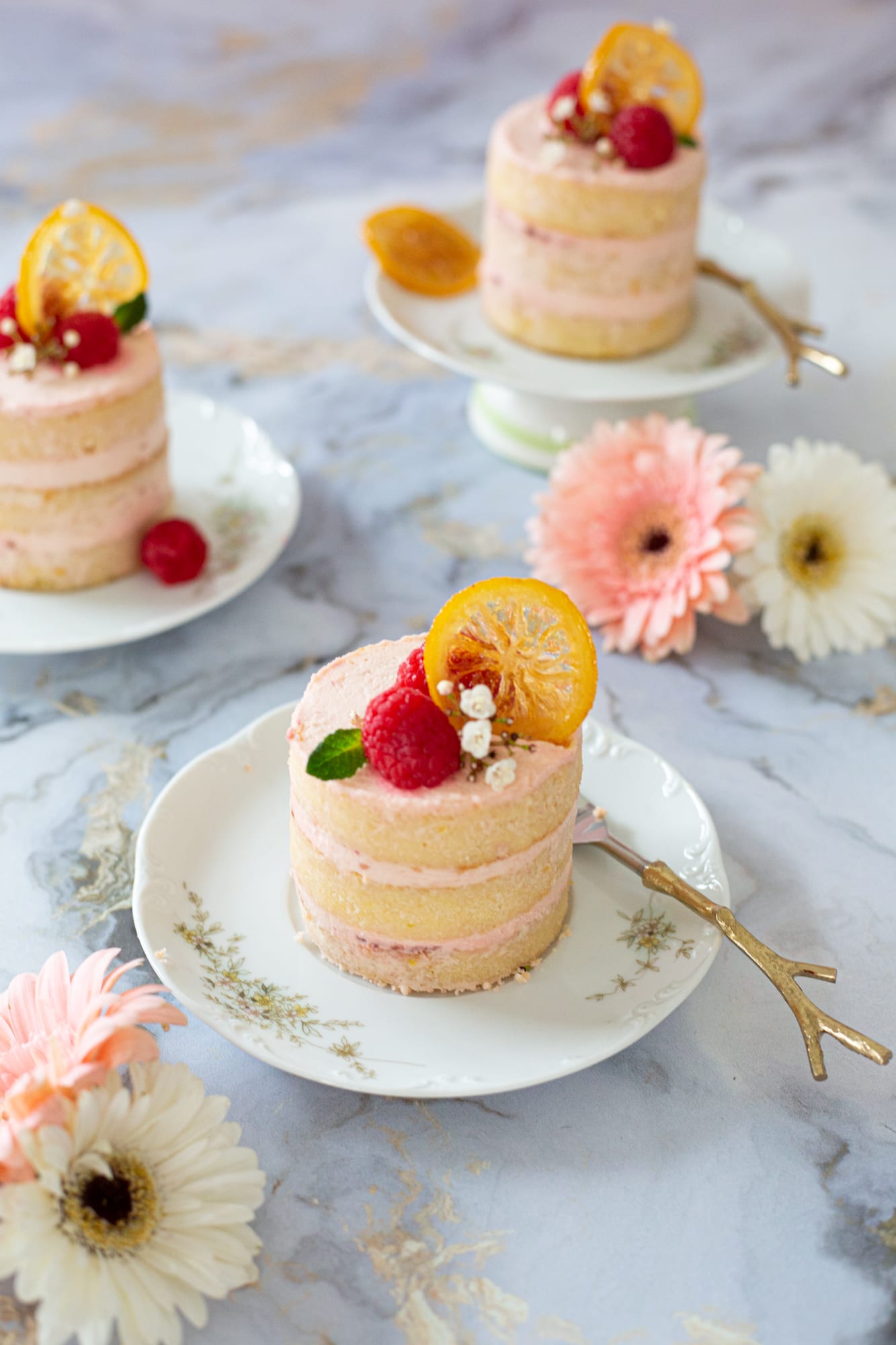 Two raspberry and lemon mini cakes with pink gerberas on marble, from above