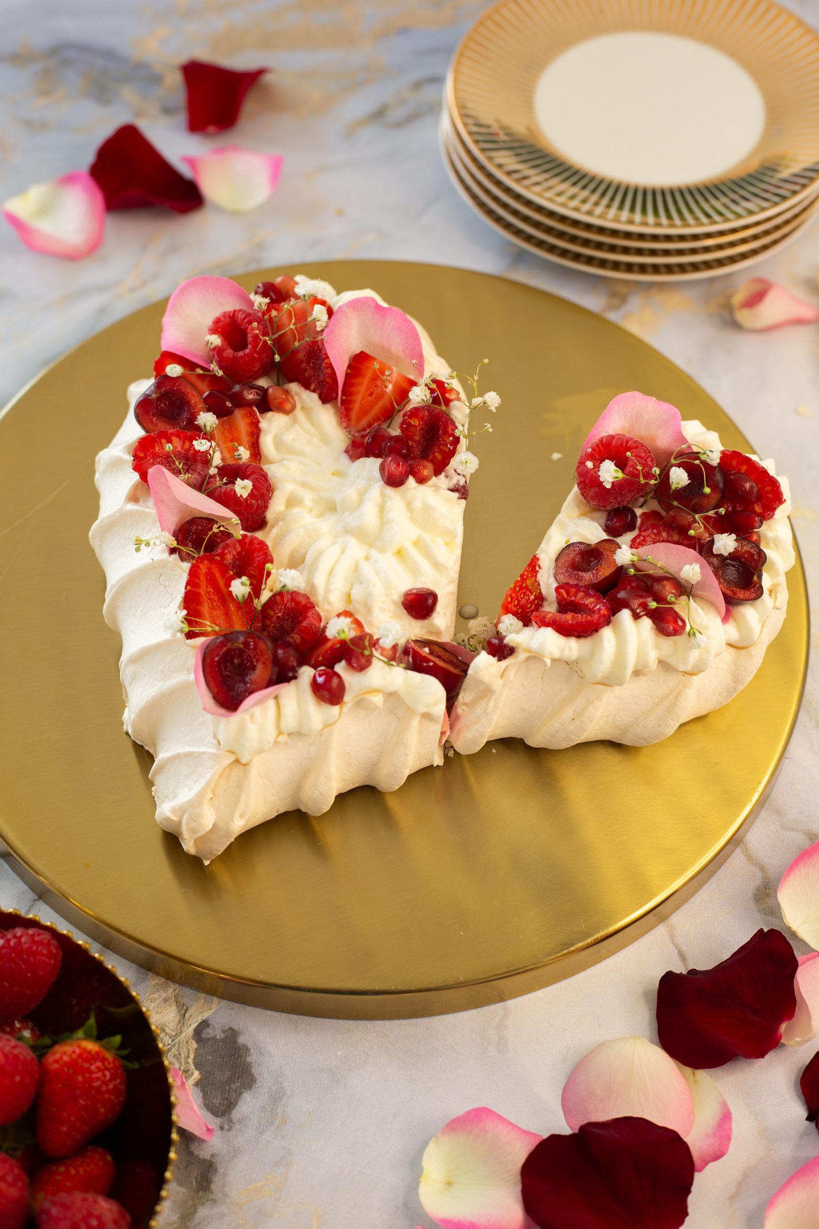A heart-shaped berry pavlova with a wedge cut out for serving, from a high angle