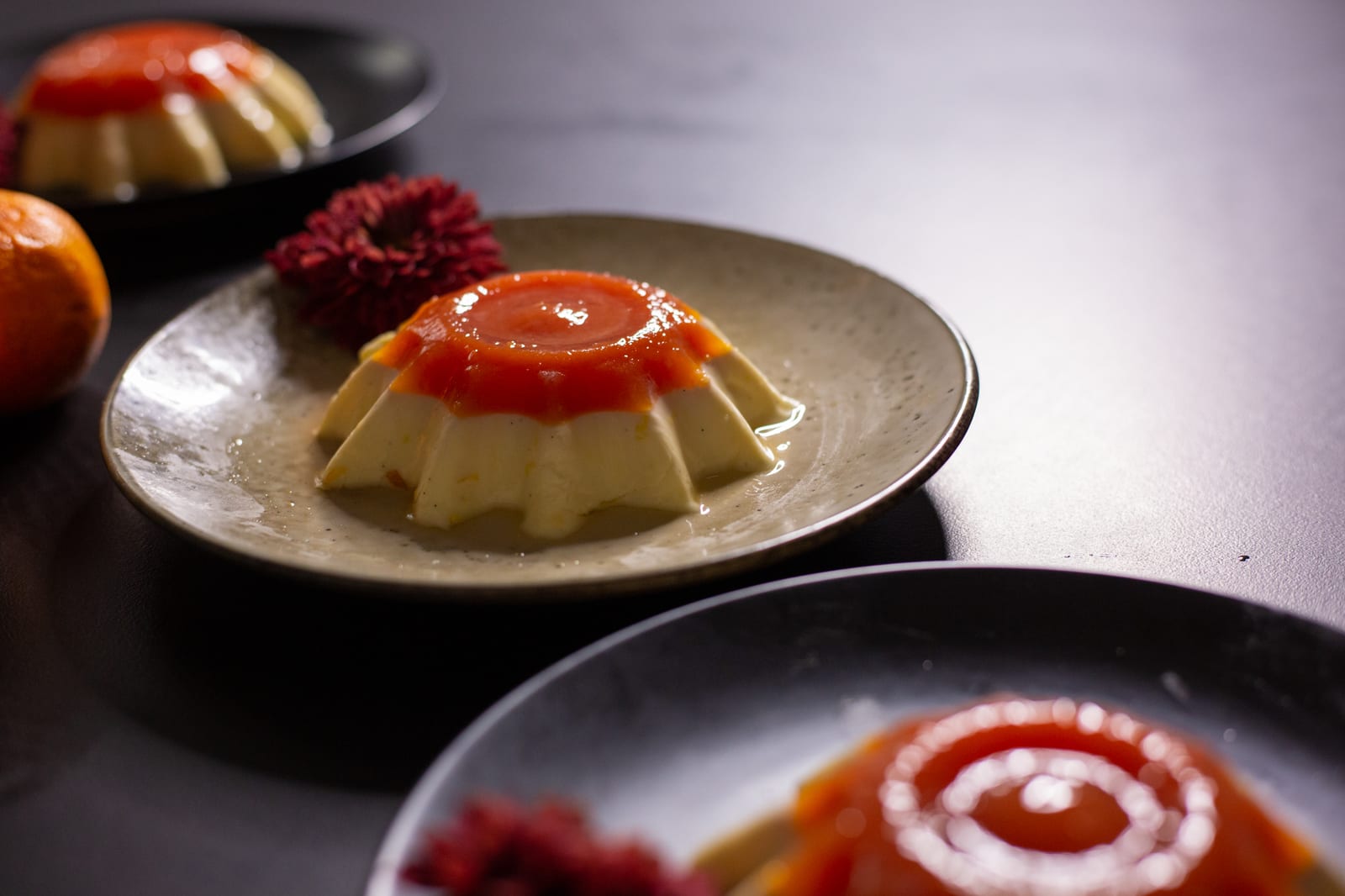 A vanilla yoghurt panna cotta with blood orange jelly on a beige plate, another blurred in front