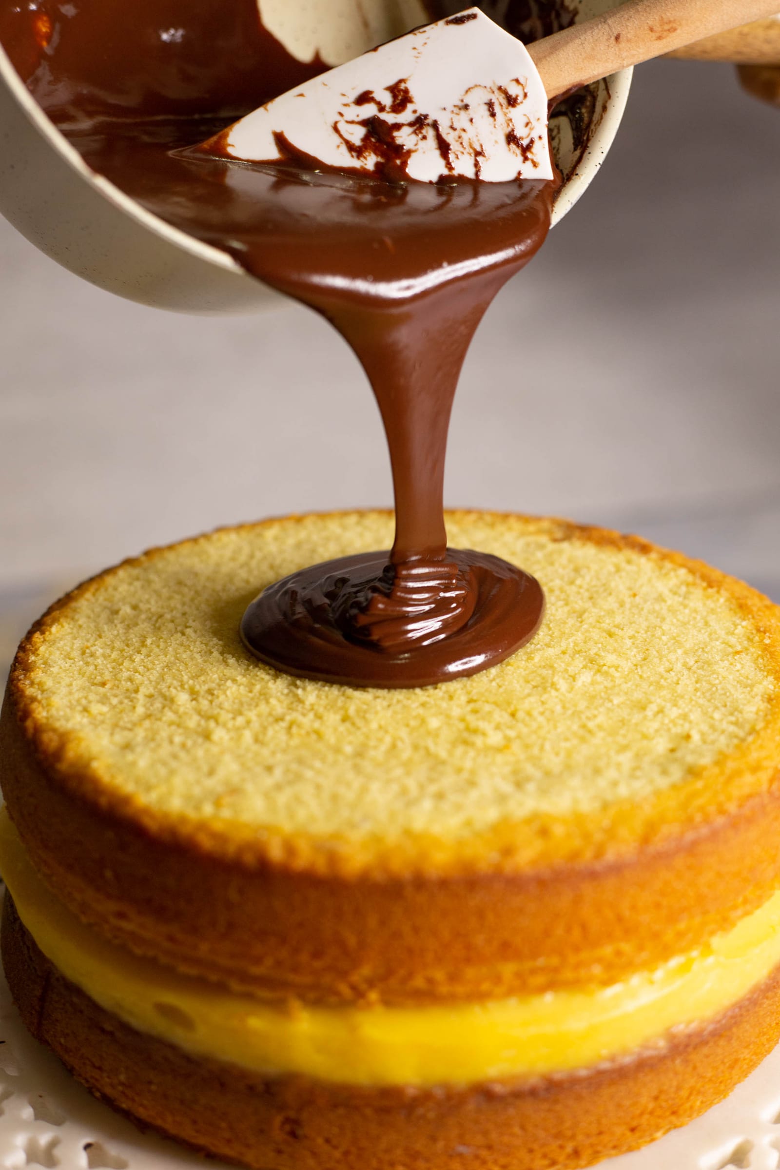 Chocolate ganache pouring onto the top layer of vanilla sponge
