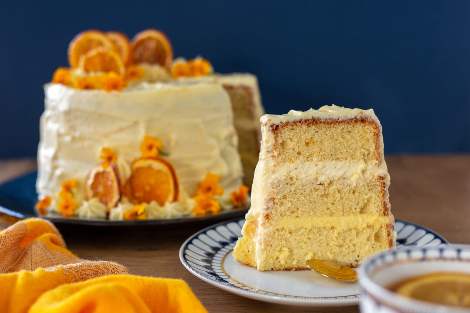 An orange cream chiffon cake with a slice cut out beside it, against a navy wall