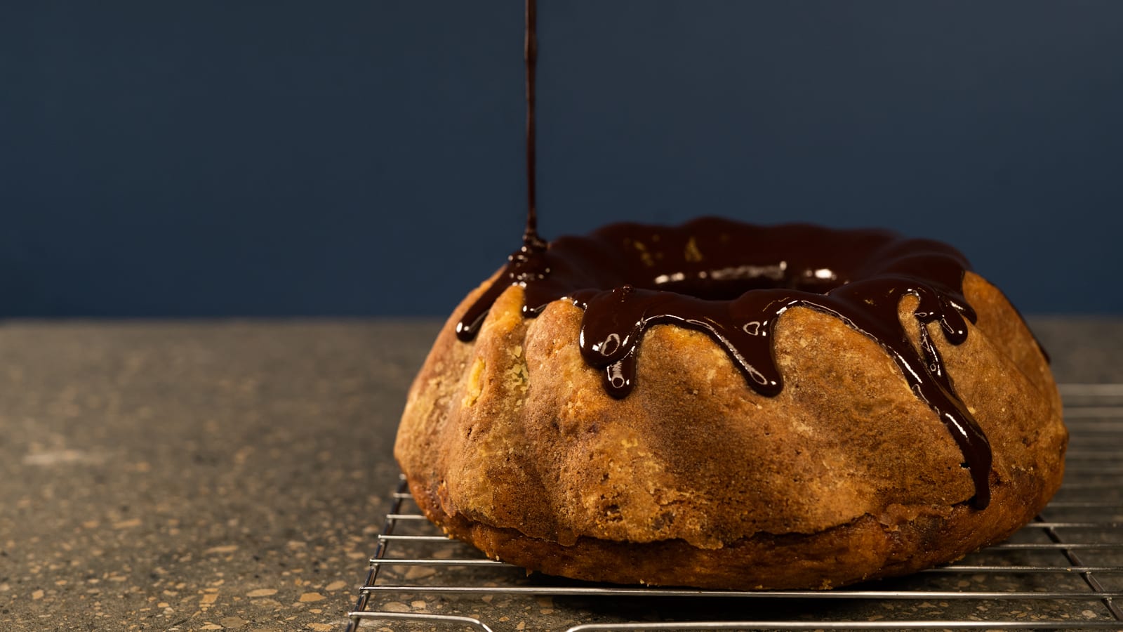 Water ganache being poured over a whole banana cake on a wire rack