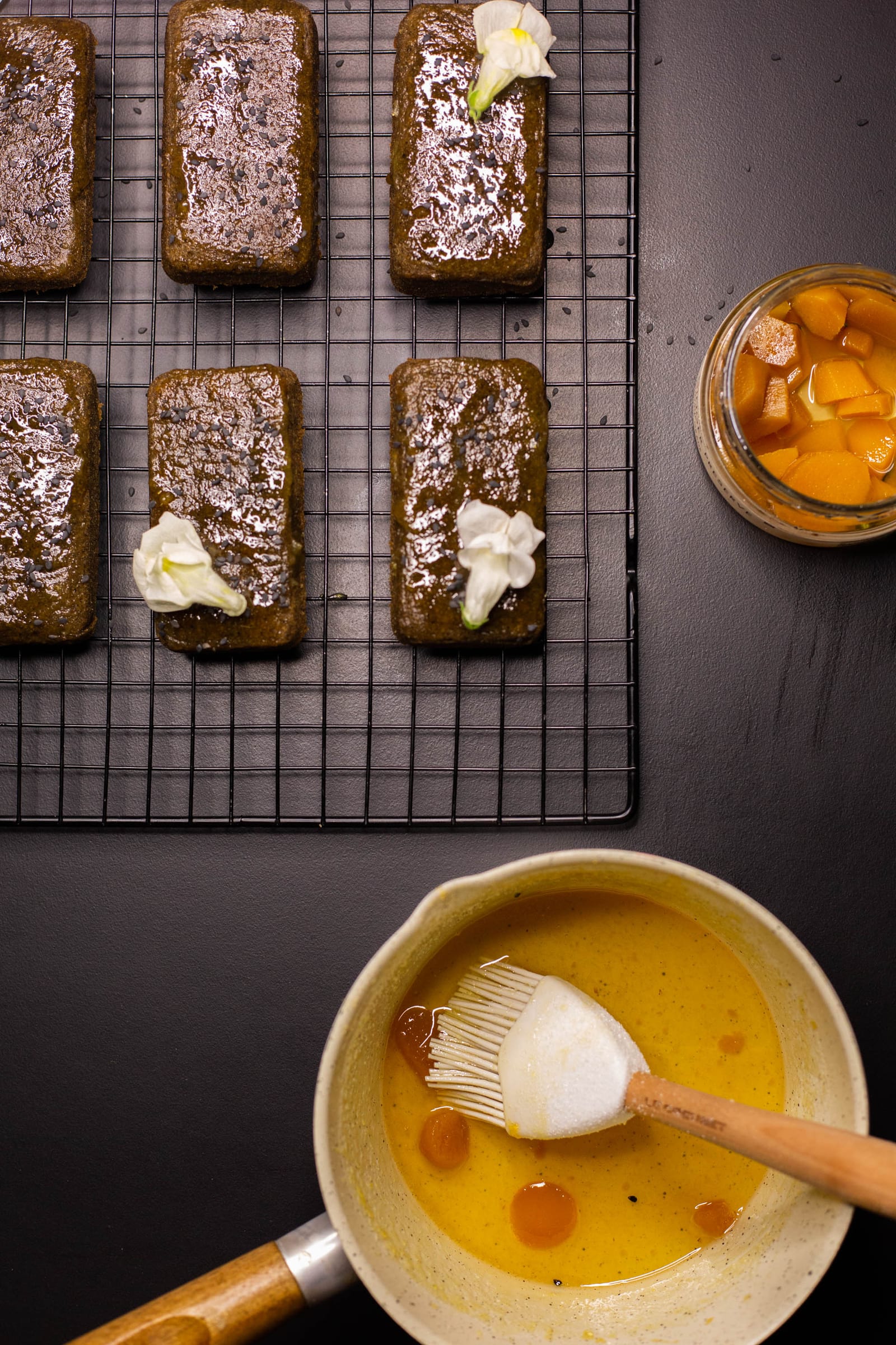 Black sesame and ginger financiers on a rack above a bowl of glaze and a pastry brush