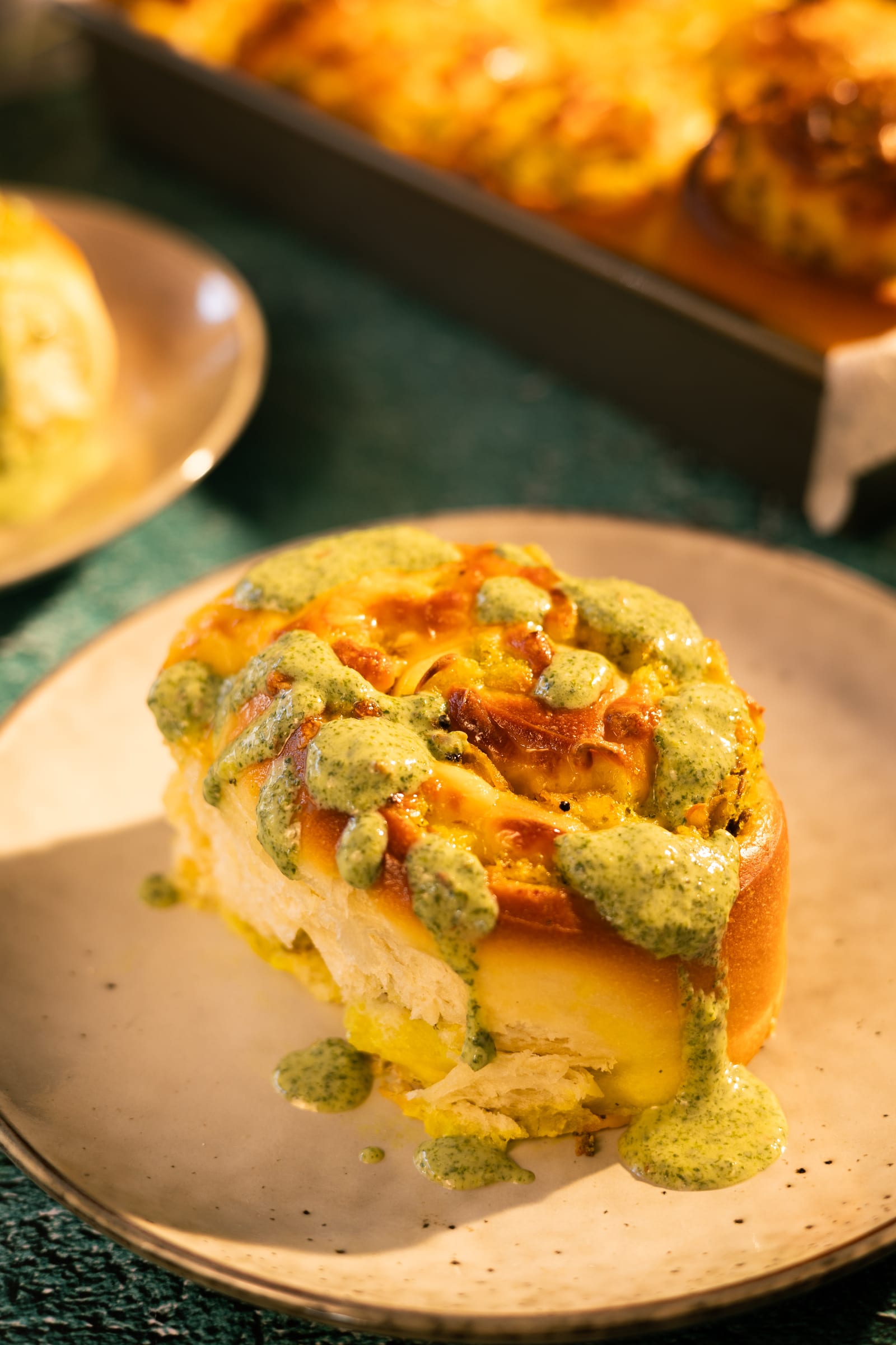 A cheesy potato scroll topped with green chutney on a plate