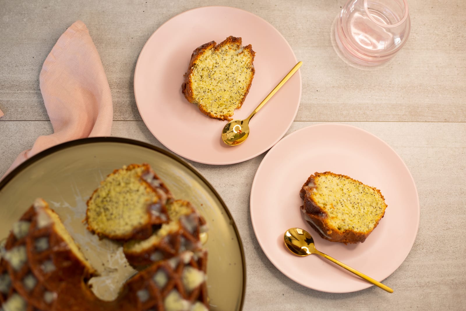 Slices of lemon, poppyseed and olive oil bundt on pink plates with gold forks, from above