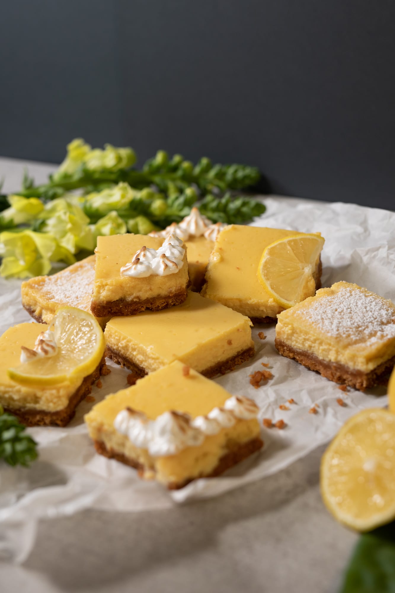 A stack of sweet and tart lemon squares beside snapdragons and a lemon