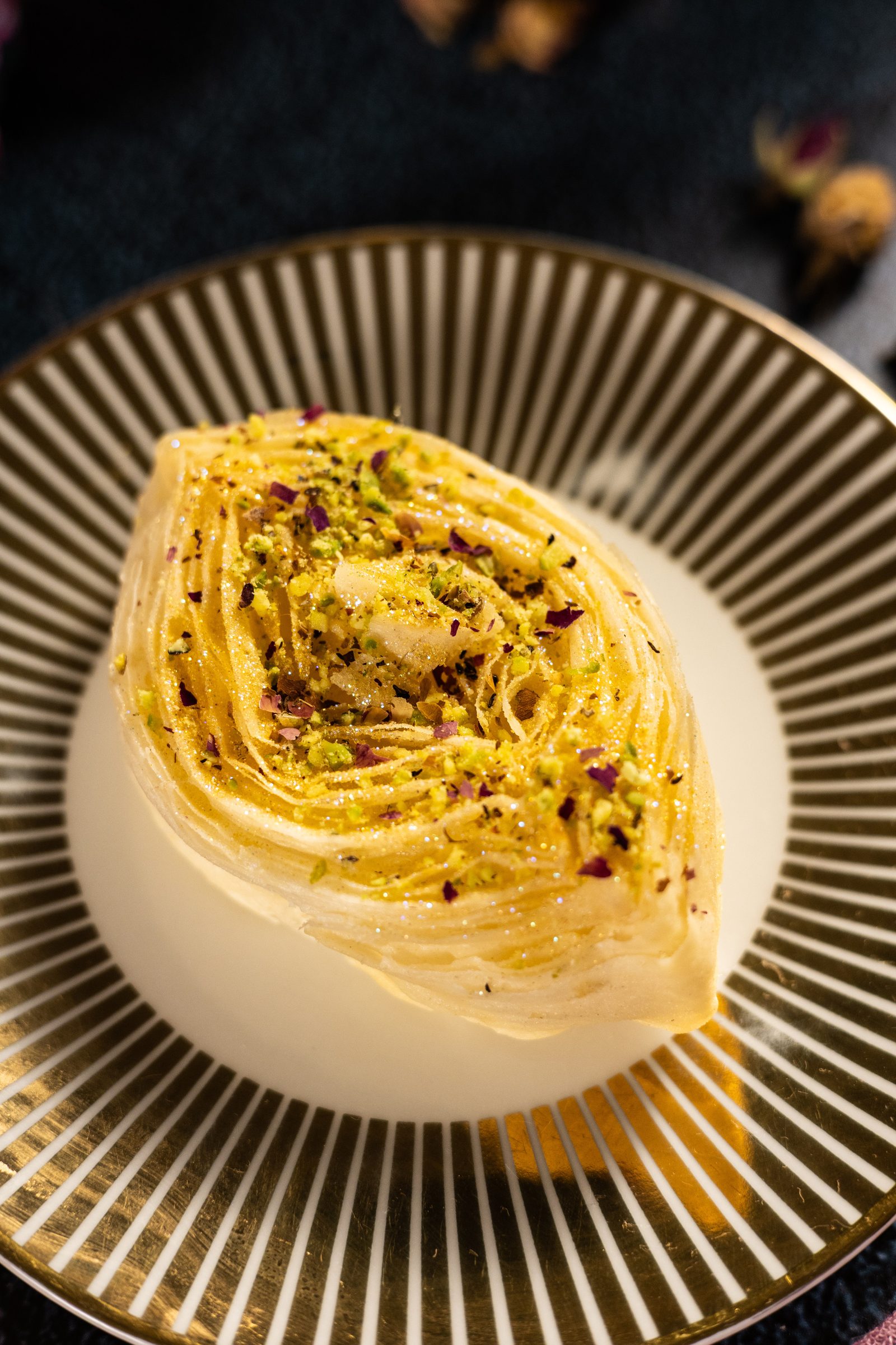 A banana puri topped with pistachios on a striped gold plate