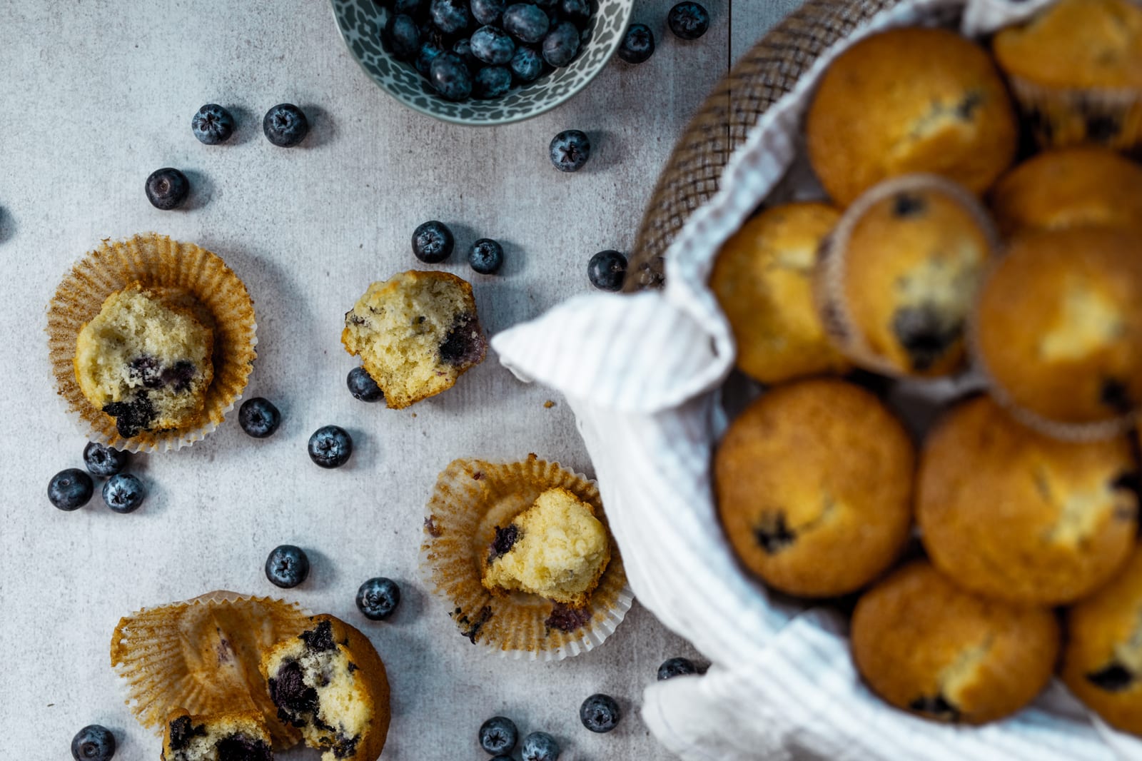 A basket of one bowl blueberry muffins beside muffins broken open to show the blueberries, from above
