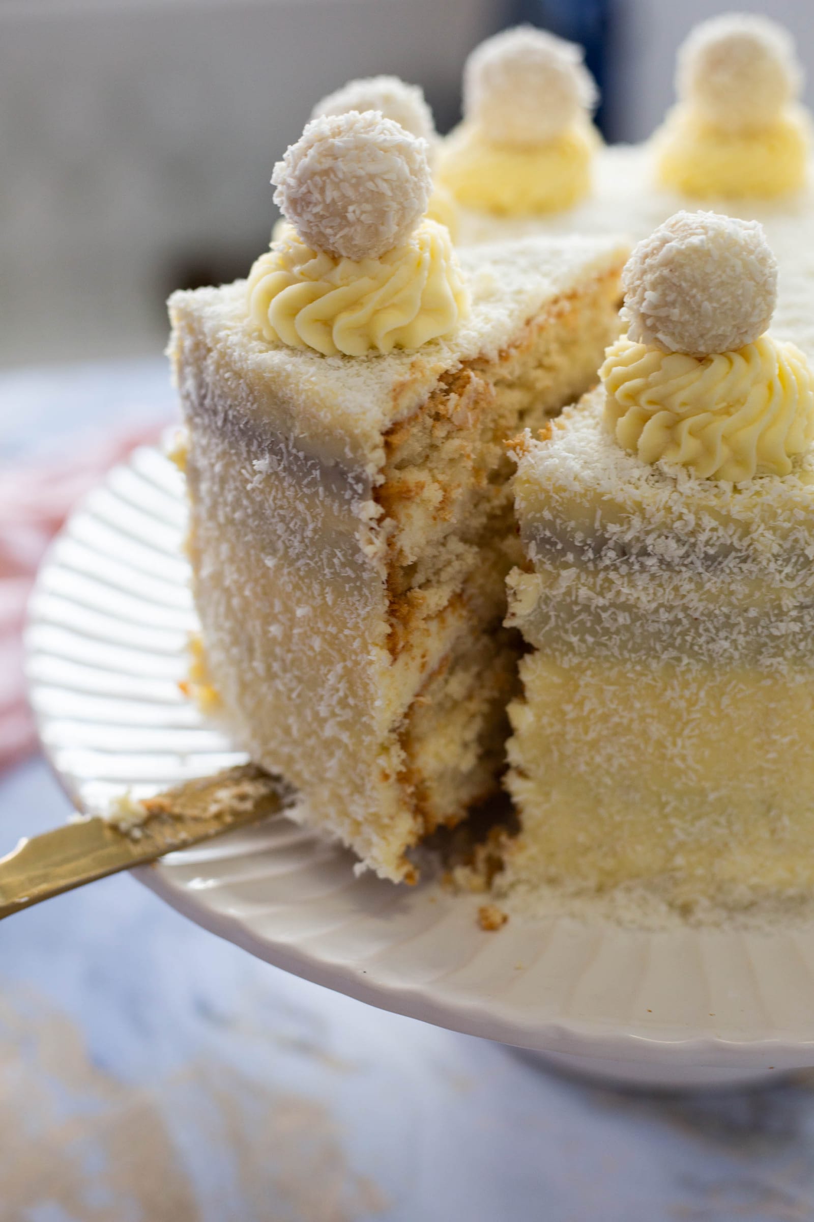 A Raffaello cake with a slice taken out, showing the layers of sponge, ganache and almond cream