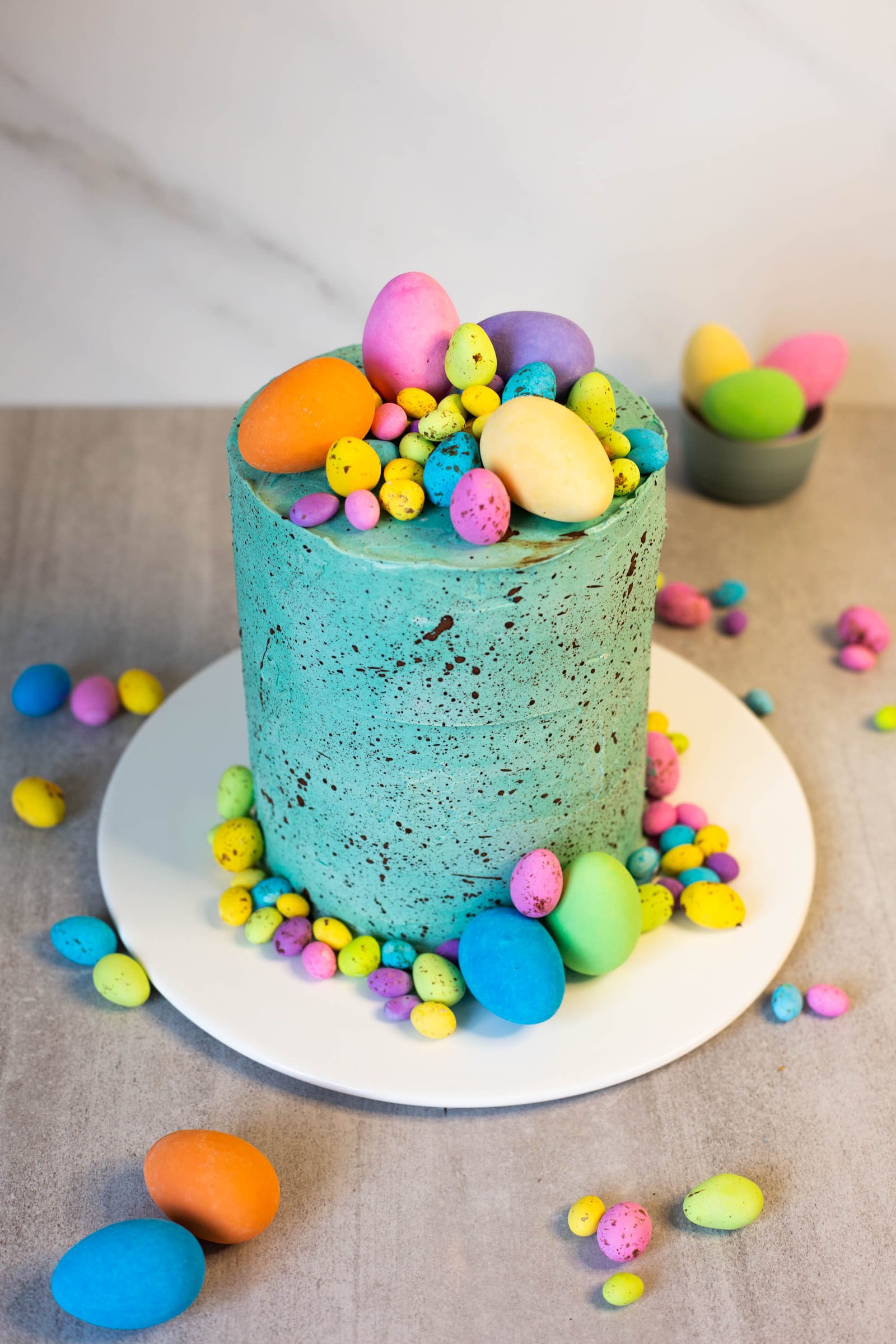 A whole speckled egg cake with speckled eggs around its base, from slightly above