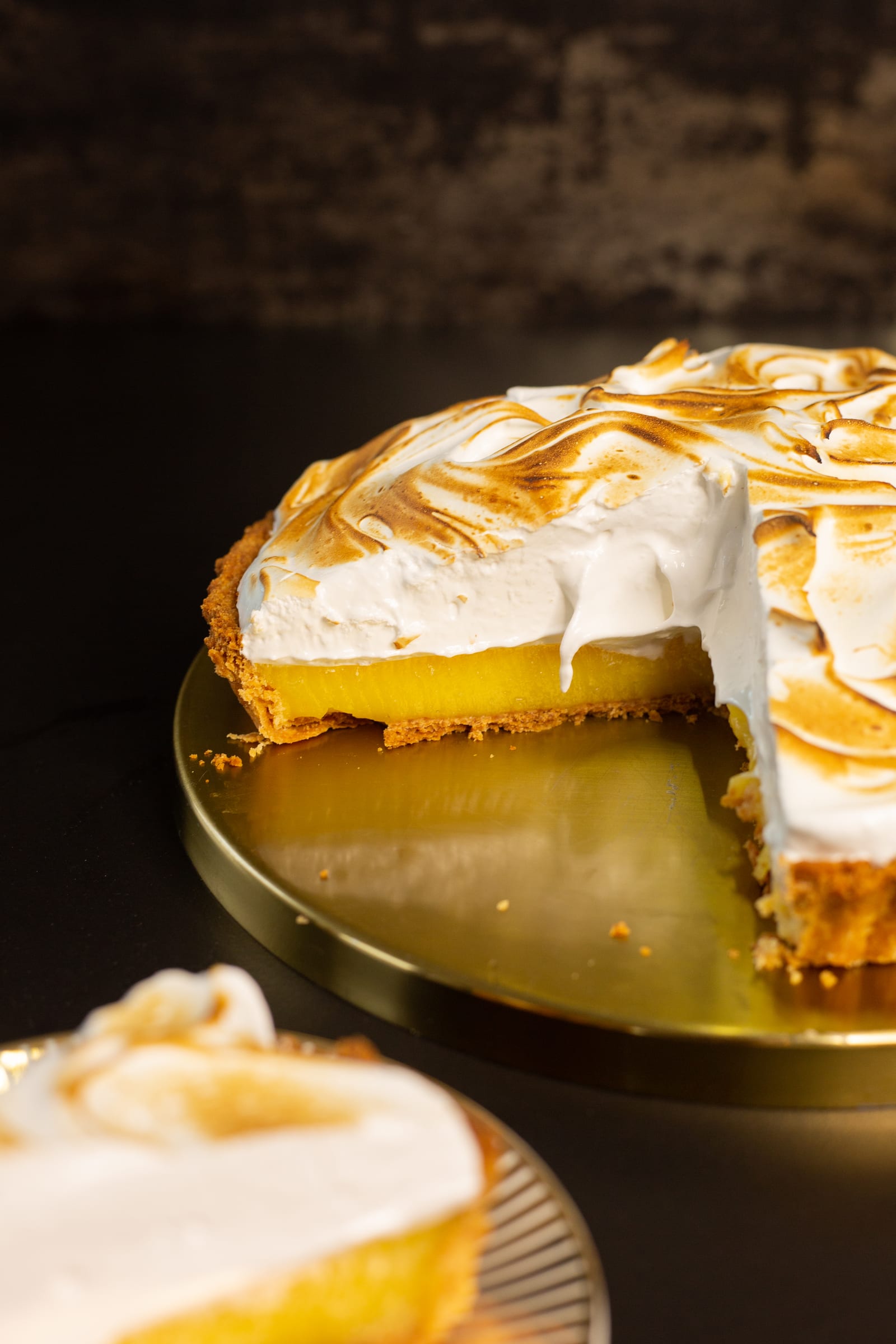 A slice of lemon meringue pie in the foreground with the cut pie behind