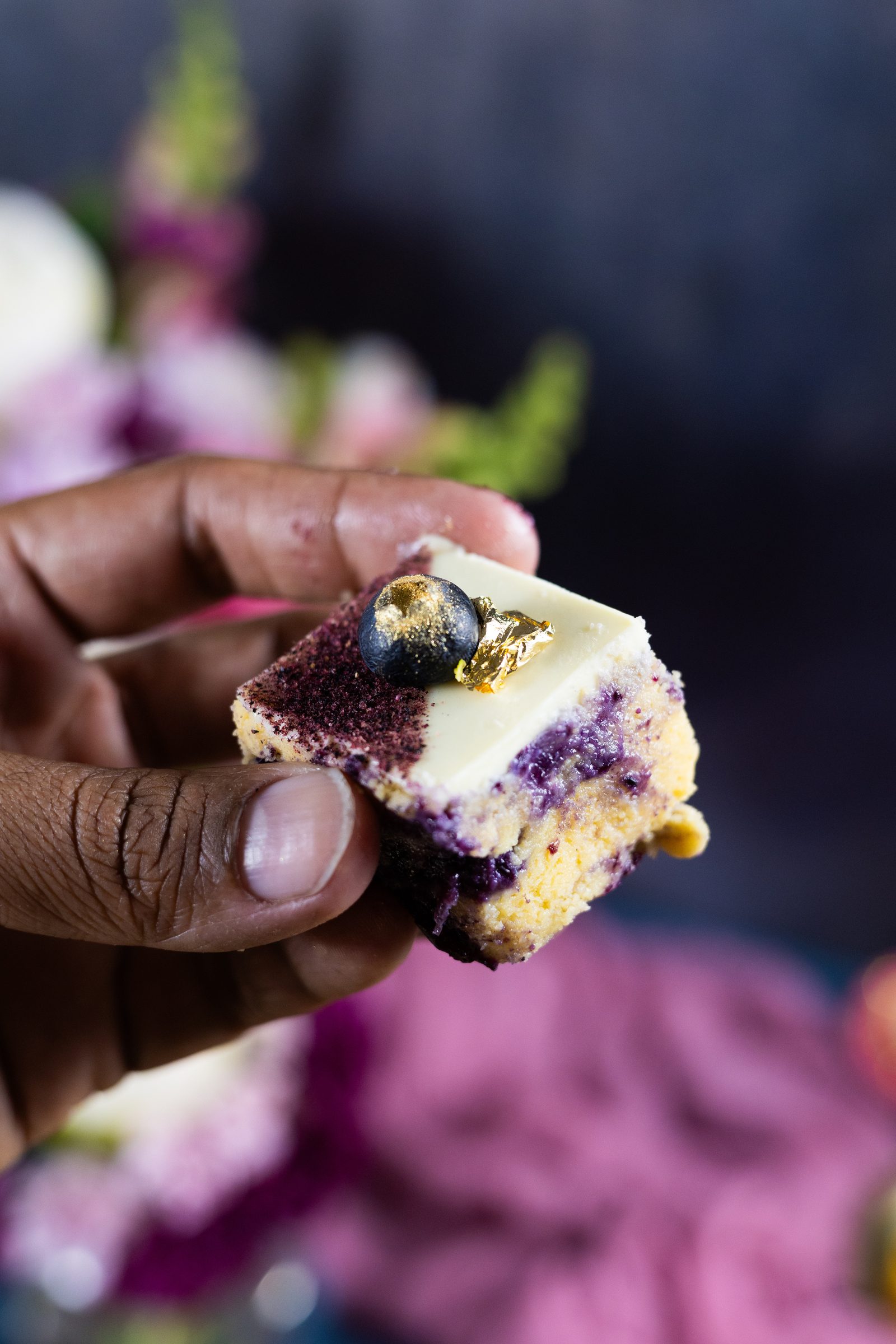 A hand holding a piece of blueberry ripple burfee, showing the purple swirl through the inside