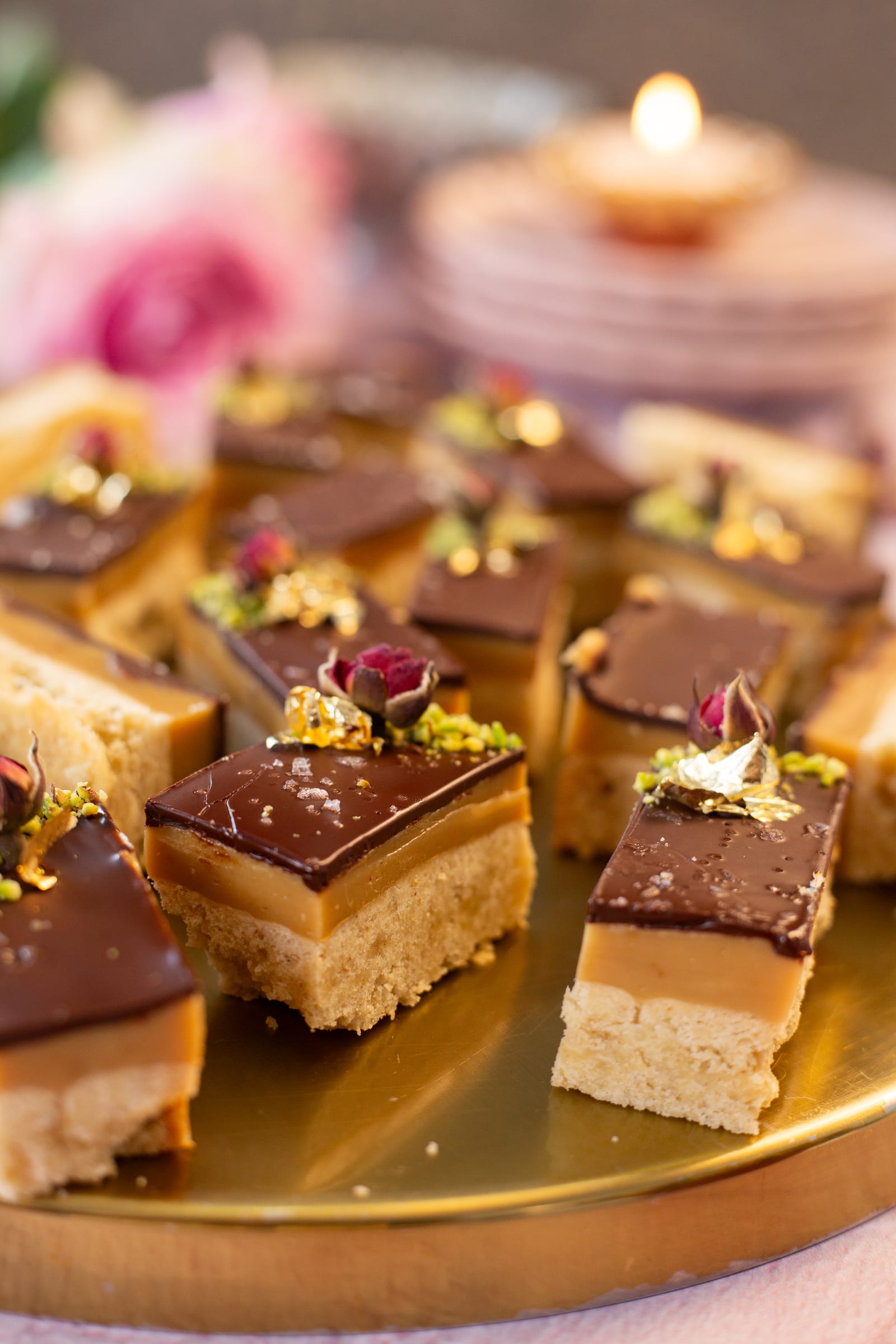 Close-up of shortbread, caramel and dark chocolate layers topped with rose and pistachio