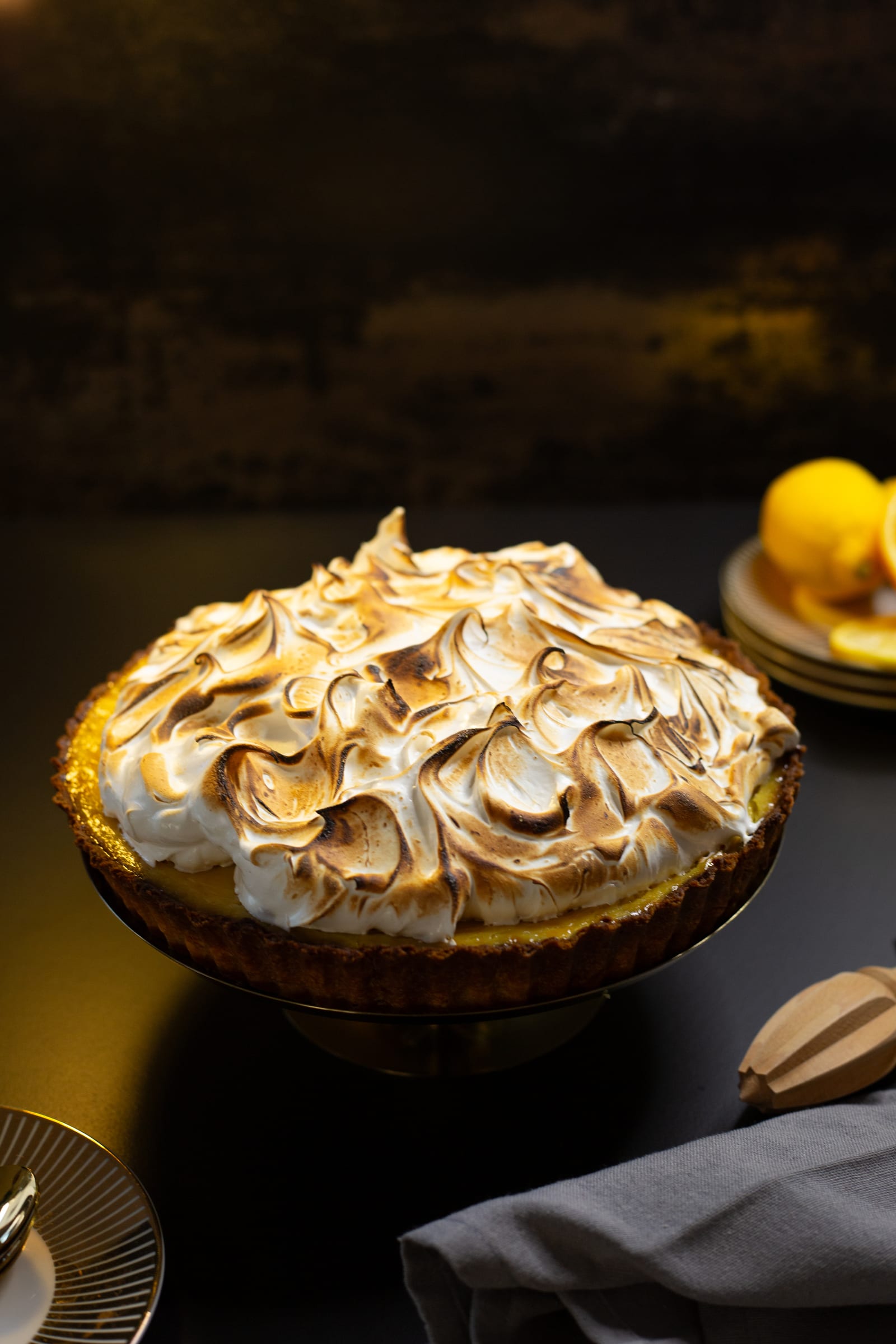 A lemon meringue pie on a dark table, with lemons