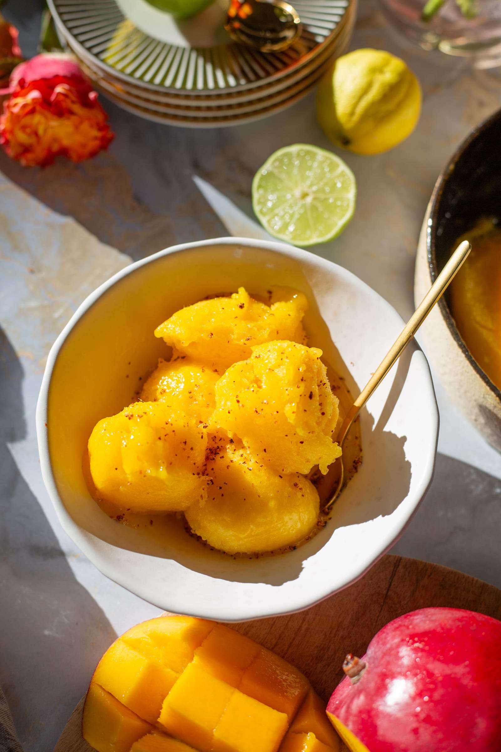 A bowl of mango and chilli sorbet scoops dusted with chilli from above, with limes and a pomegranate