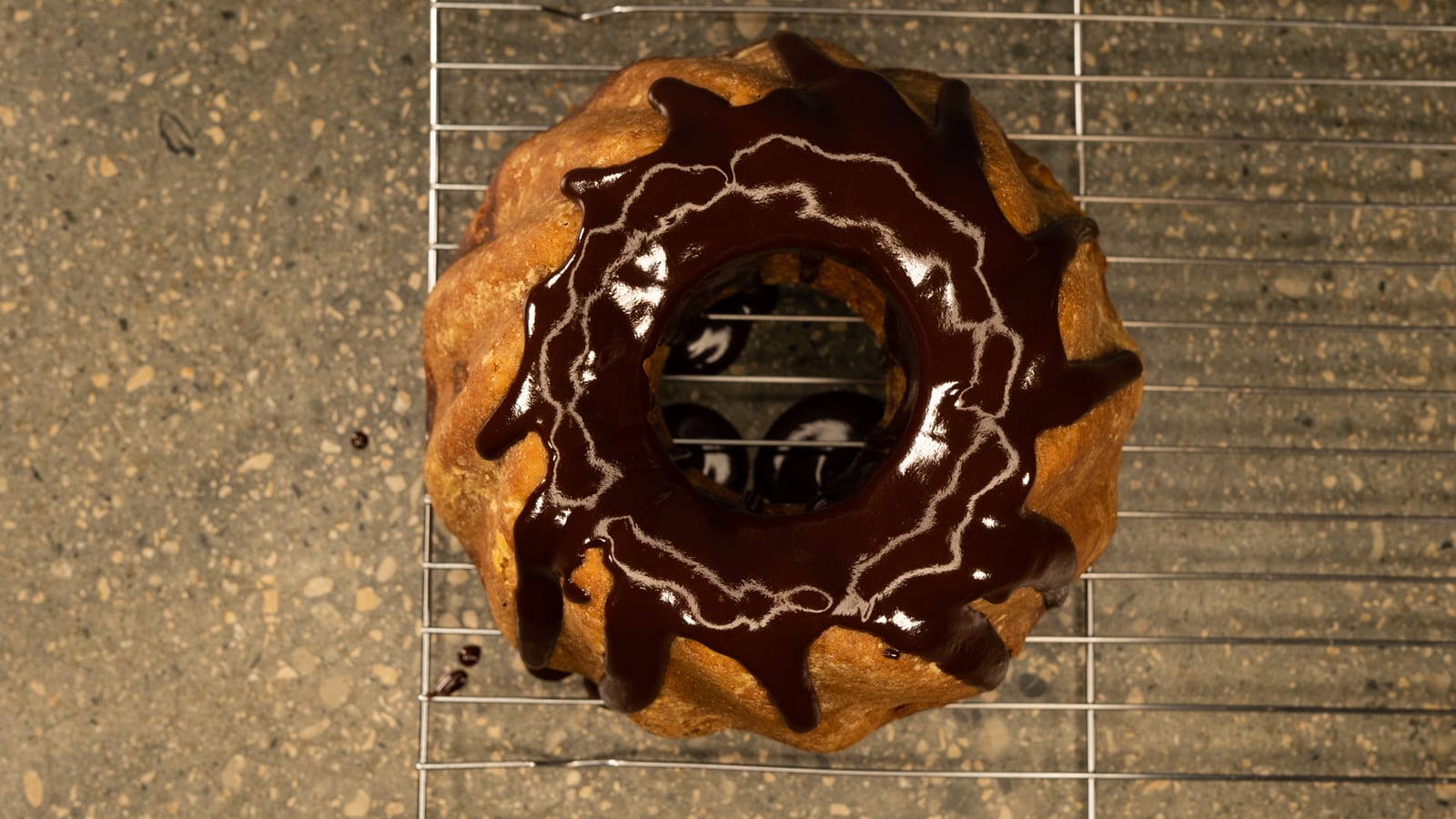 A banana cake with a ring of water ganache drips on a wire rack, from above