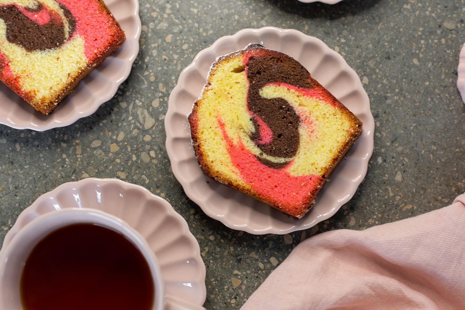 Slices of Neapolitan pound cake on scalloped pink plates beside a cup of tea